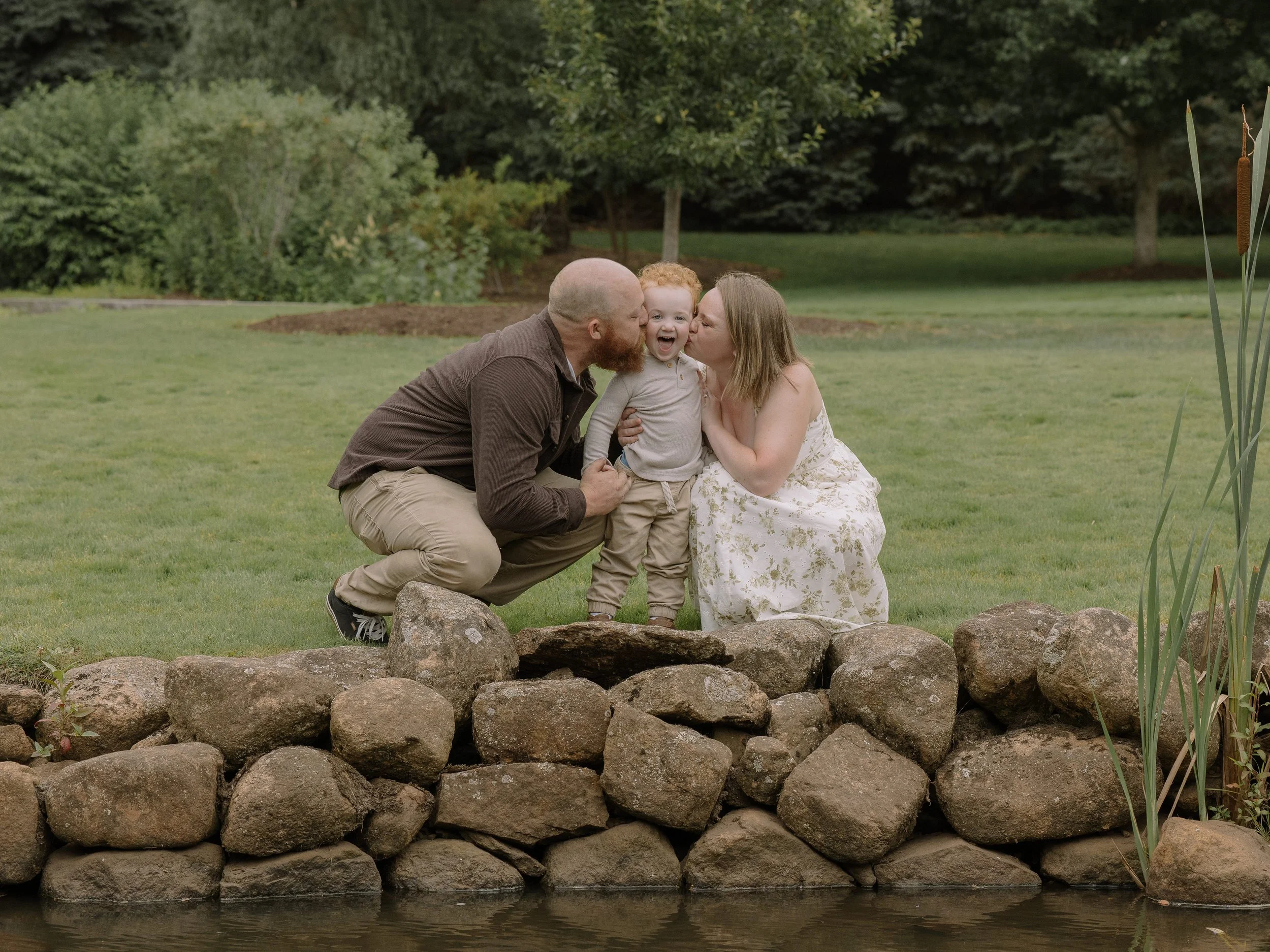 Mom and dad with young red haired toddler boy in a grassy park
