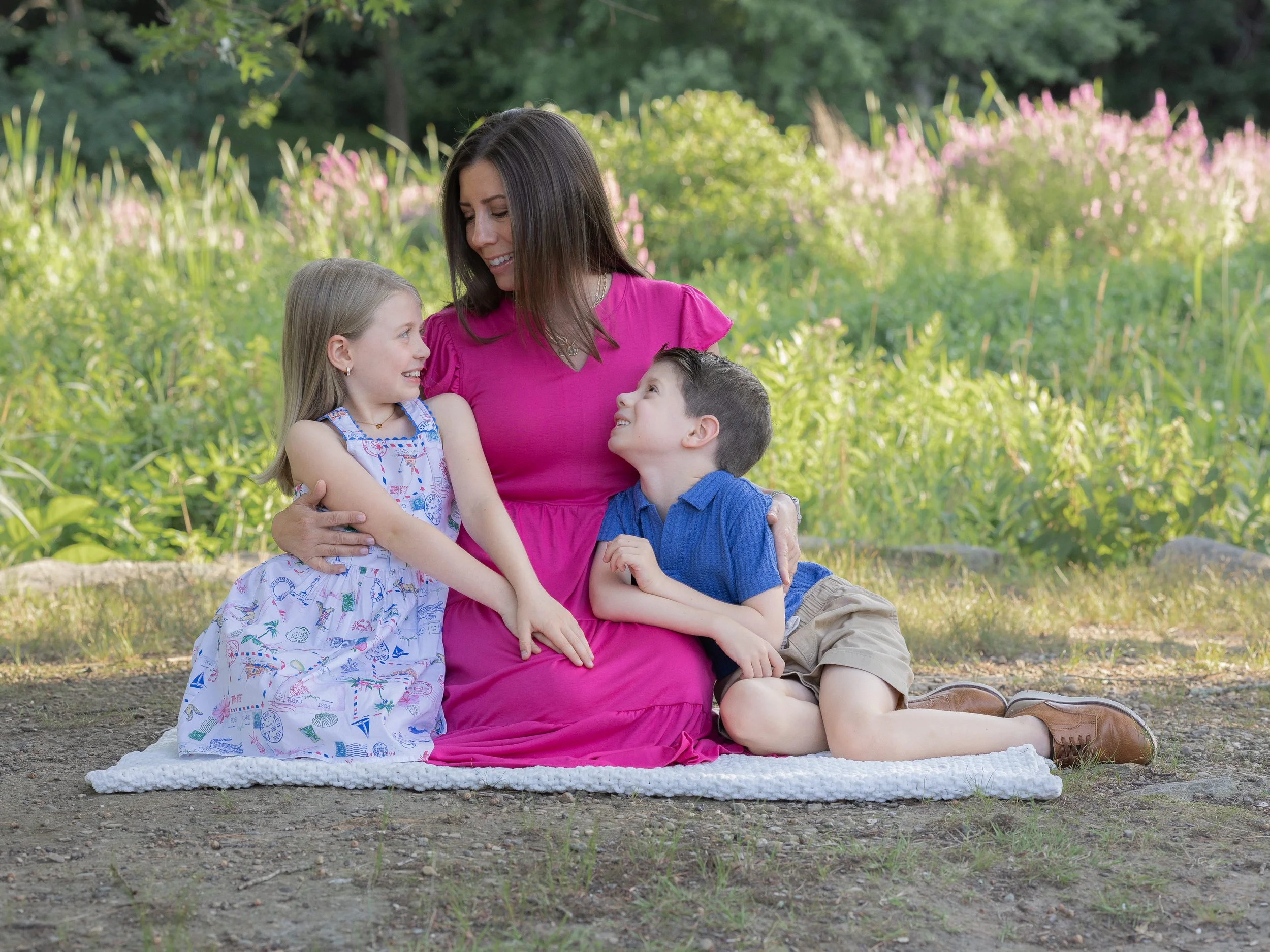 Mother in pink dress with two young kids in front of a flower field