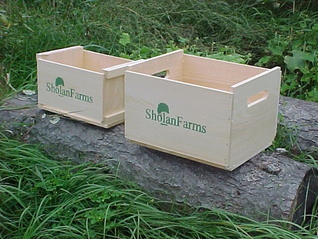 Two wooden crates with the Sholan Farms logo placed on a log outdoors, surrounded by green grass and plants.