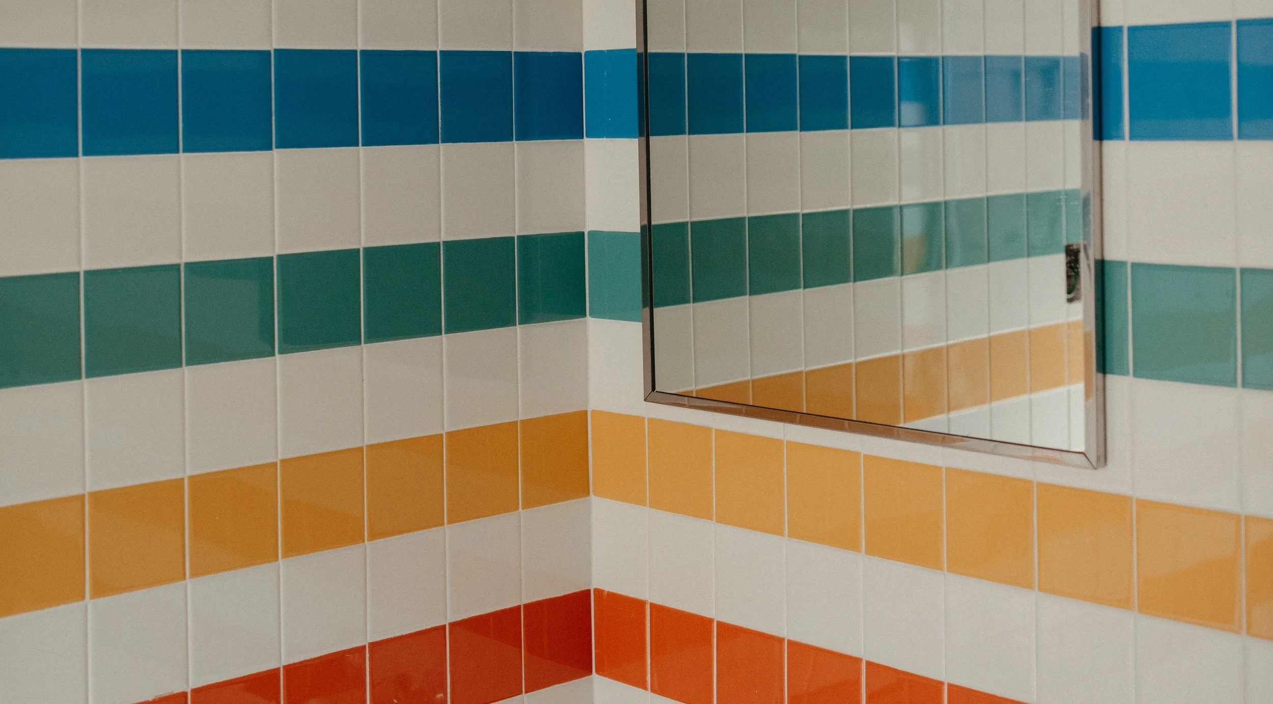 Colorful tiled restroom wall with a rectangular mirror reflecting similar tiles.