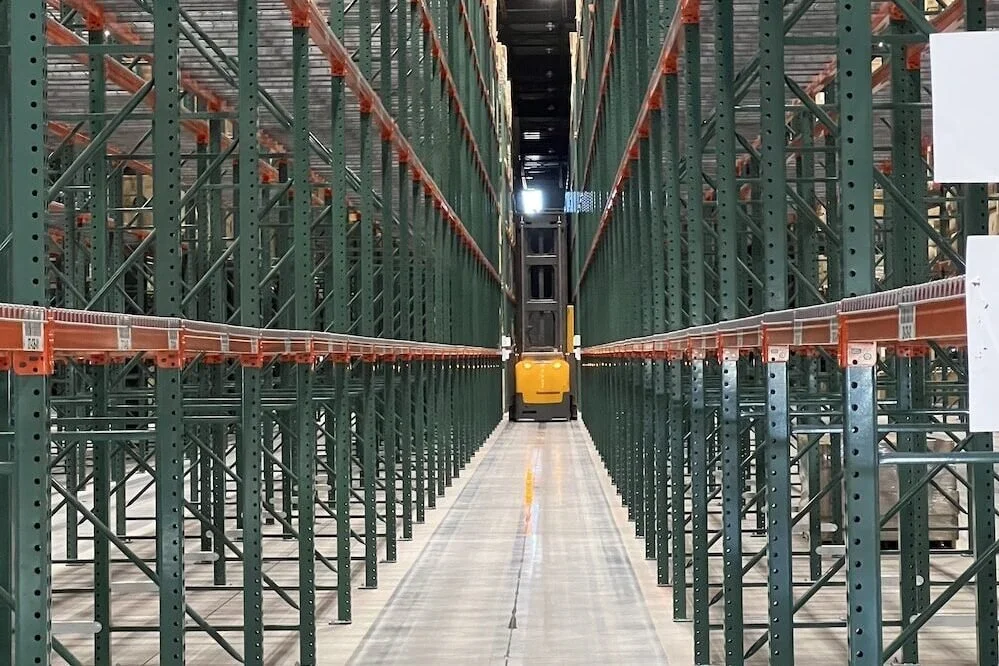 Empty warehouse storage racks with a yellow and black forklift in the aisle.