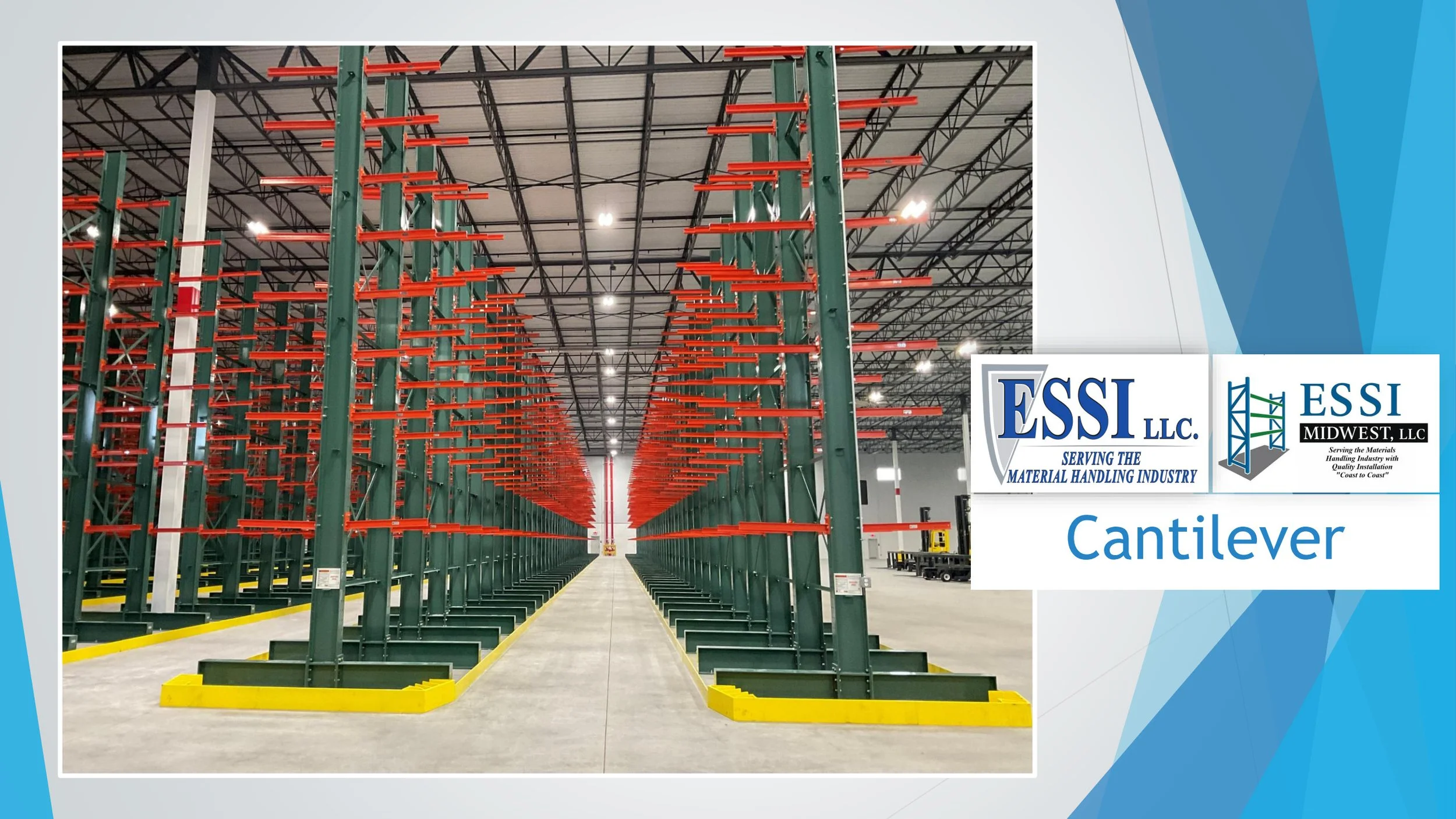 An empty industrial storage warehouse with tall green racks that have orange beams, arranged in rows along a central aisle with yellow safety barriers at the end of each row.
