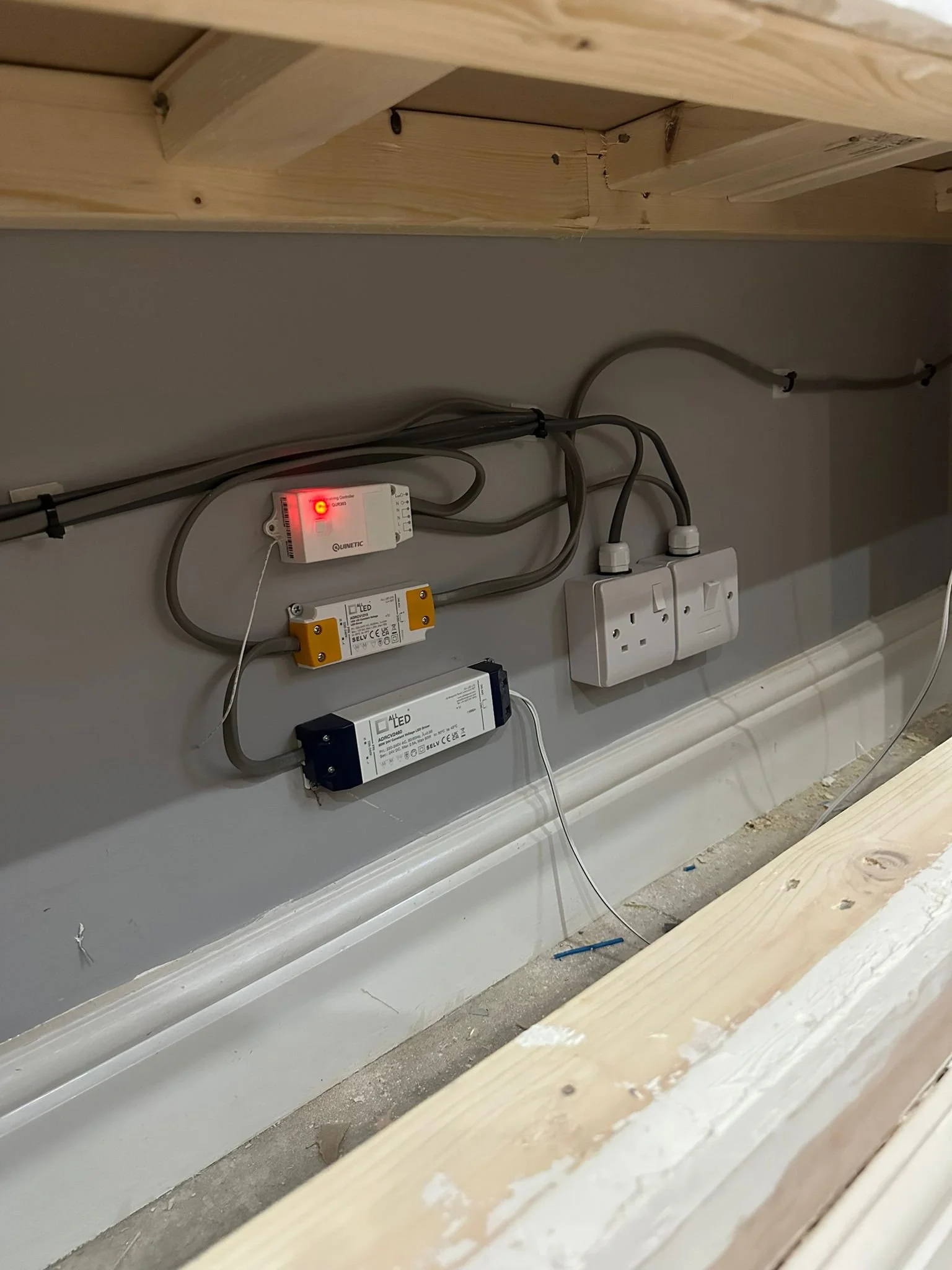 Electrical wiring and power outlets installed behind a wall, with some construction materials visible in the foreground.