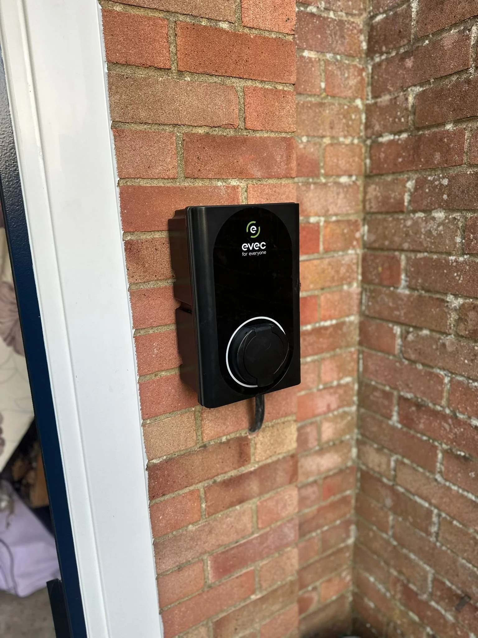 A black electric vehicle charger mounted on a brick wall outdoors, with text 'evoc for everyone' and a circular white symbol on it.