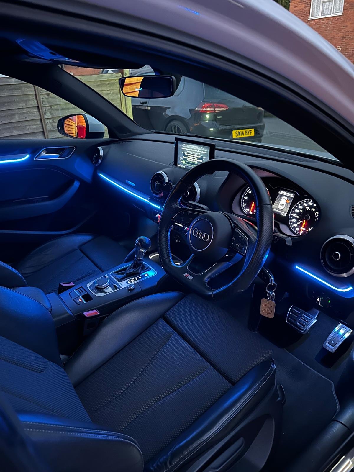Interior of a modern car with blue LED interior ambient lighting kit, black seats, and a digital dashboard display.