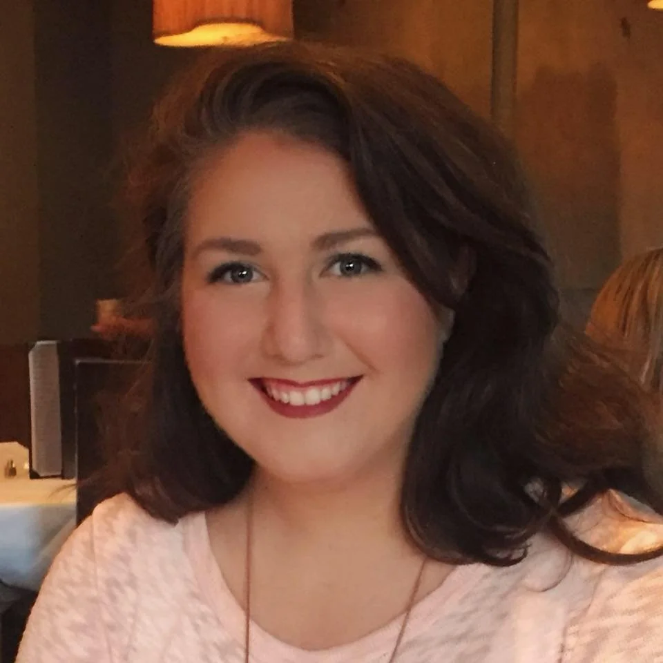 A woman with dark wavy hair smiling at the camera in a restaurant setting.