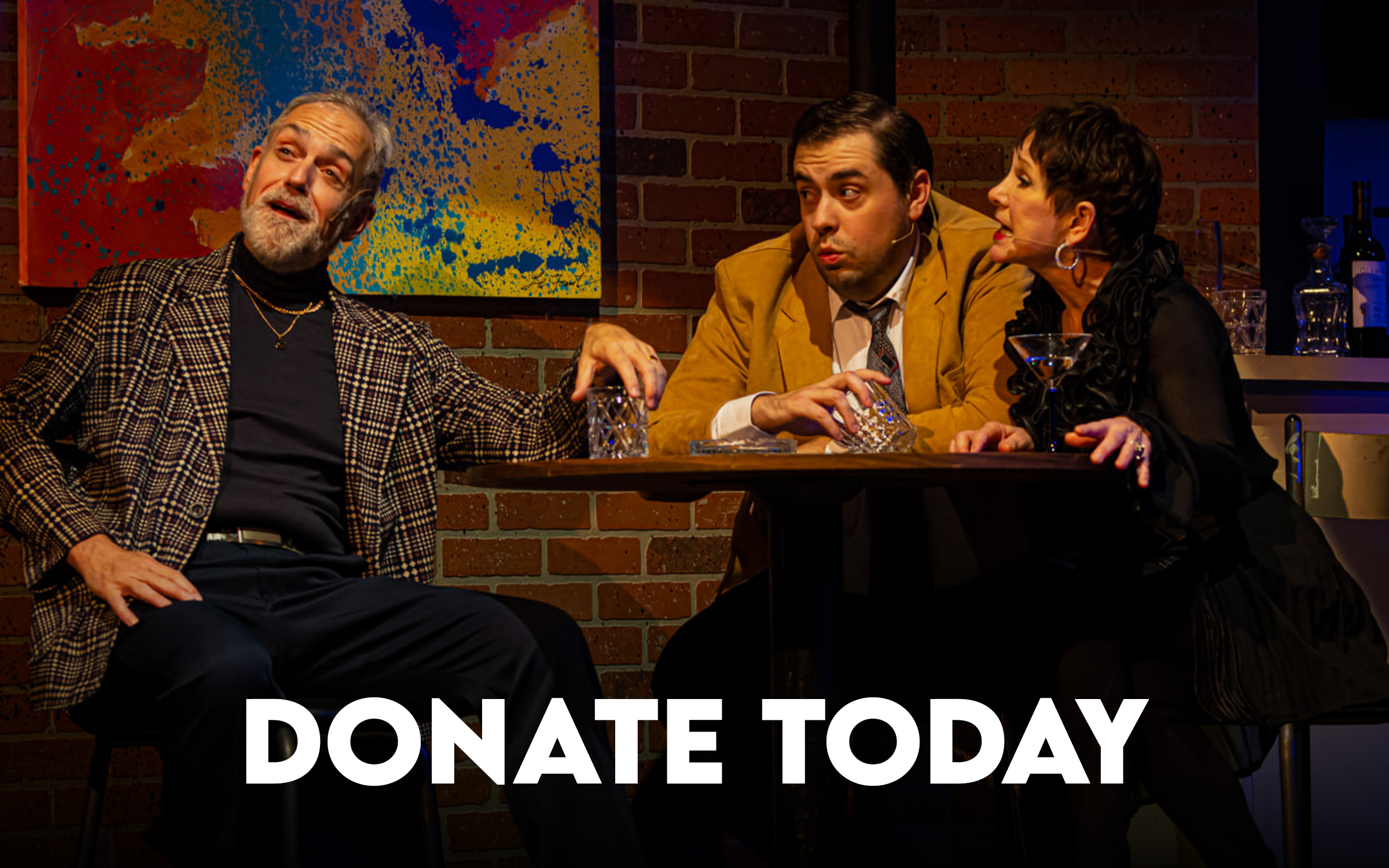 Three people sitting at a table, with a man in a plaid jacket and gold jewelry talking, and a man and woman listening, in a brick-walled room with a colorful painting. The text 'DONATE TODAY' is at the bottom.