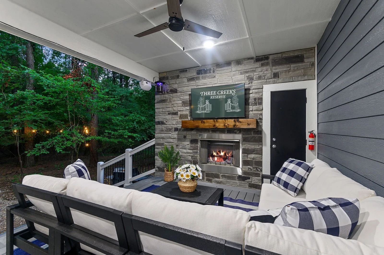 Covered porch with outdoor furniture, a fireplace, a flat-screen TV, and forest view.