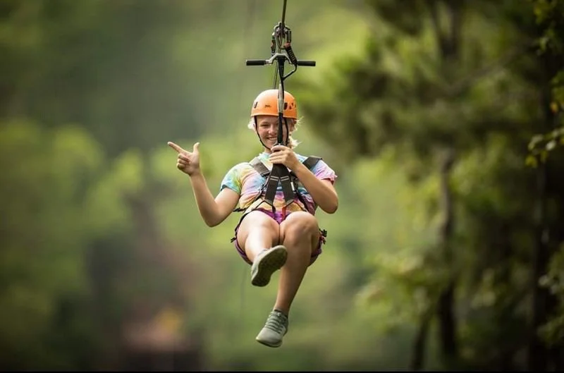 Girl in a helmet enjoying a zipline in a green forest