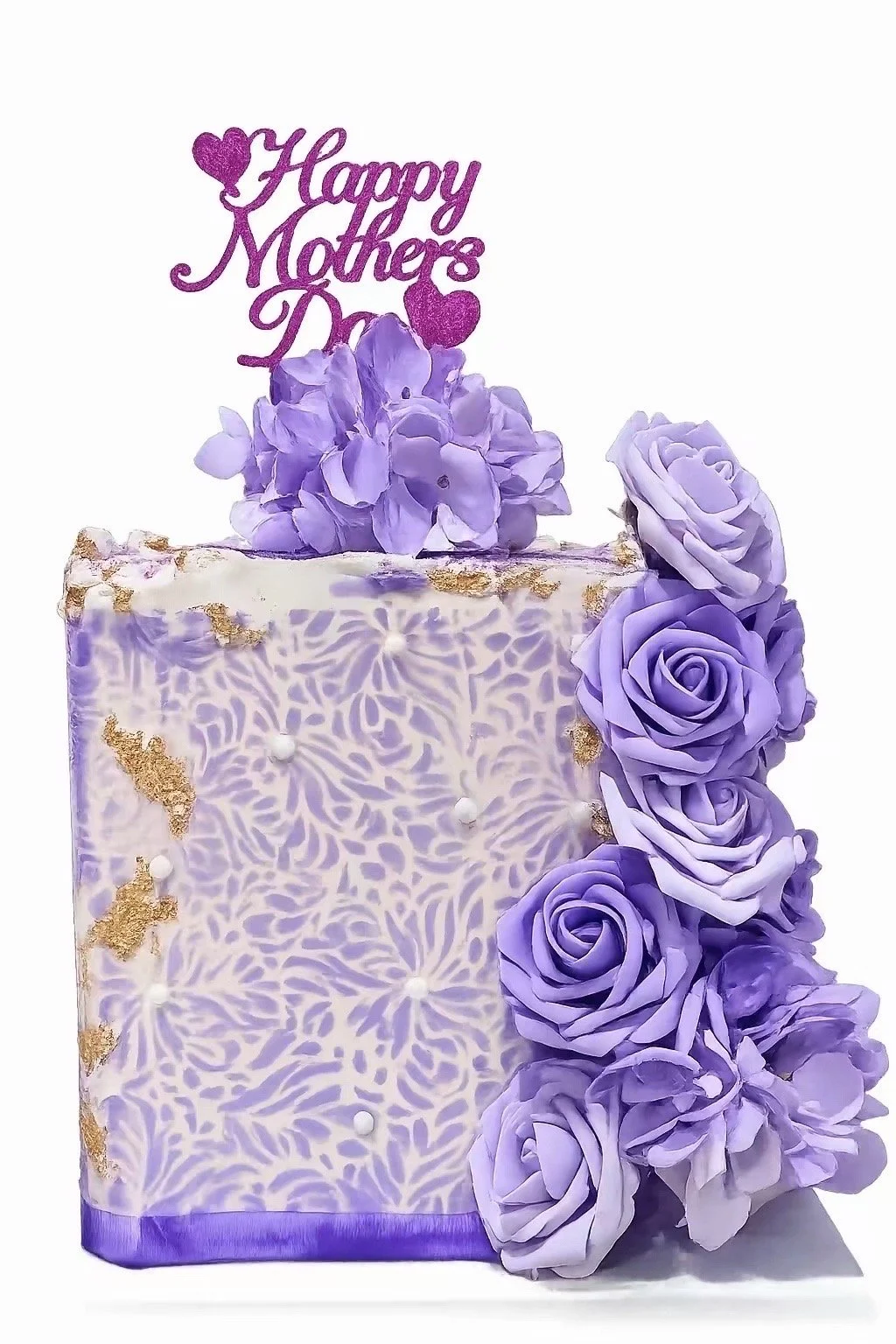 A decorative purple Mother’s Day cake decorated with purple roses and hydrangeas, with a purple and white pattern on the sides, gold accents, and a purple "Happy Mother’s Day" topper with hearts.
