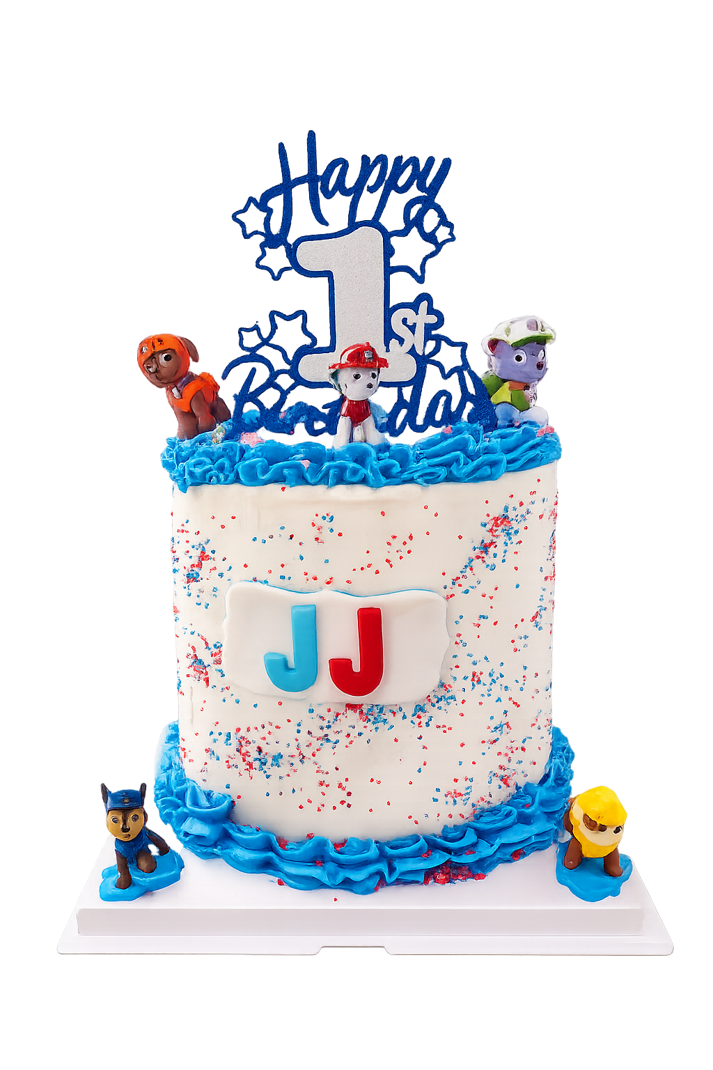 A birthday cake decorated for a first birthday with a Super Wings theme. The cake has three figurines of Super Wings characters on top, a large blue and white "1st" topper, and blue and red sprinkles. The front features a white fondant plaque with th