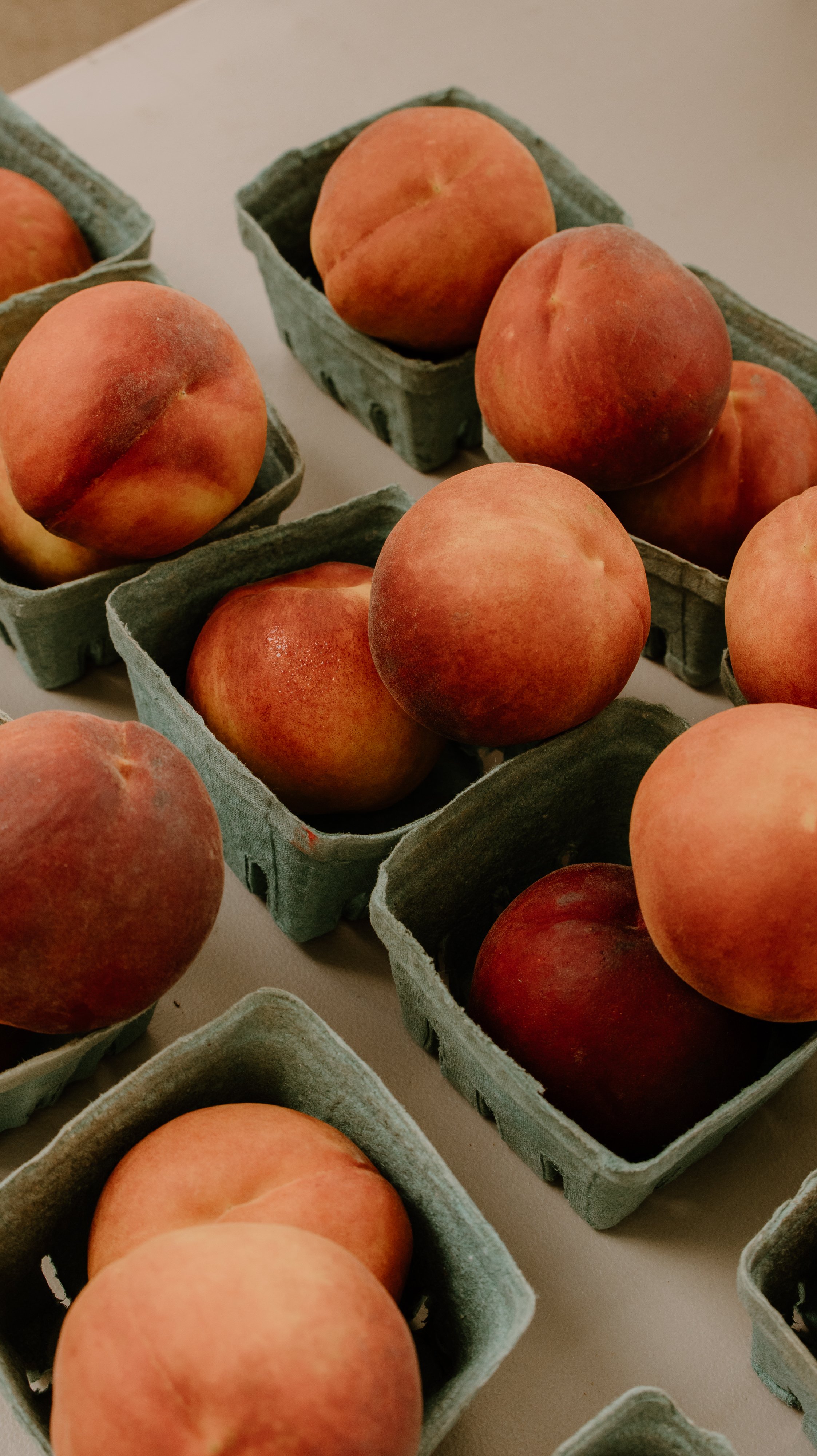 Close-up of ripe peaches in green containers on a white surface.
