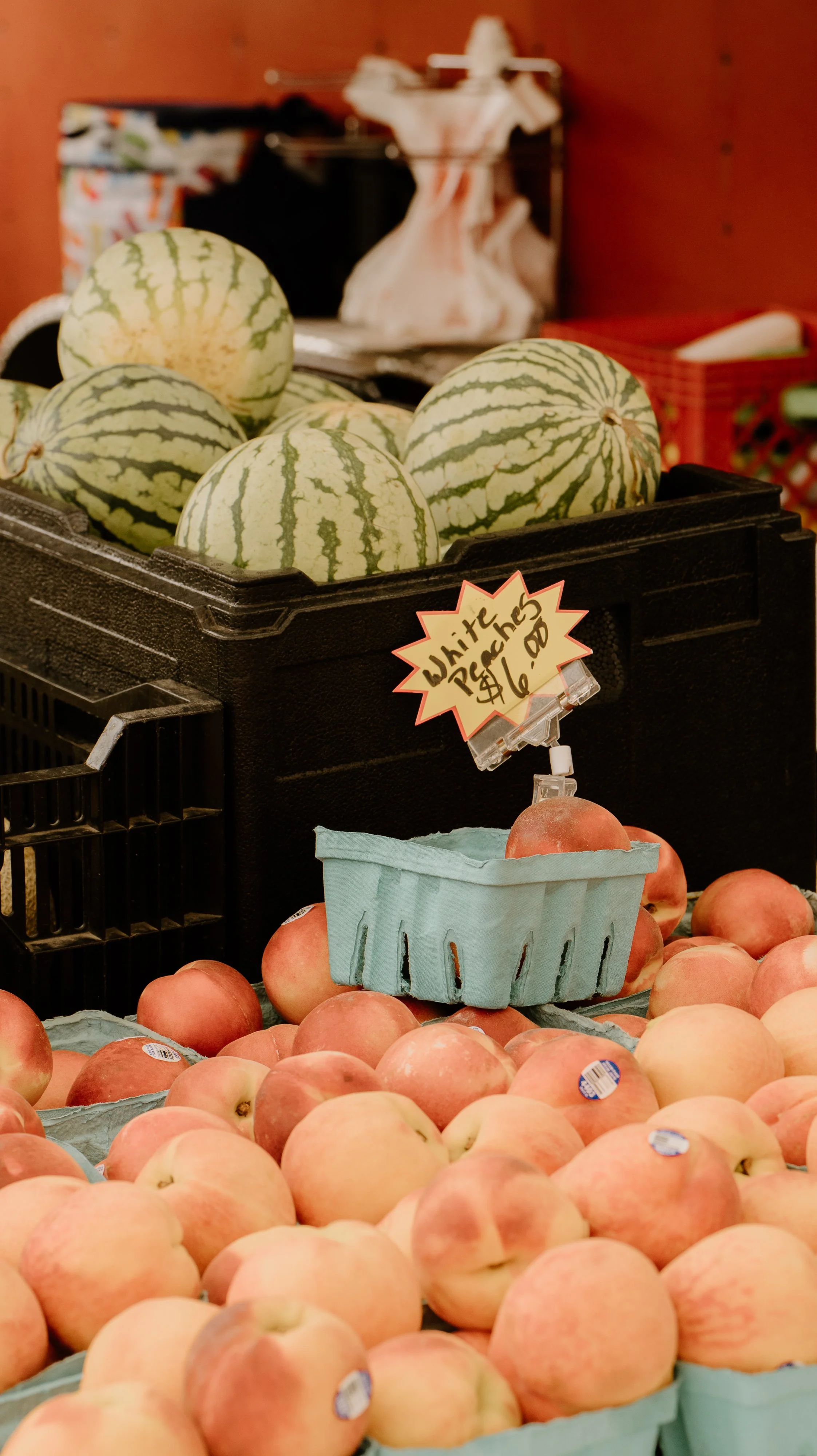 Display of peaches in baskets and watermelons with a sign indicating 'White peaches $6.00'.