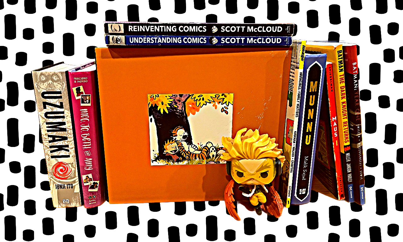 A collection of comic books and graphic novels, including titles like "Reinventing Comics," "Understanding Comics," "Munu," and "Batman the Dark Knight Returns" on a polka dot surface. There's also a decorative framed photo of a cartoon tiger and a Funko Pop! figure of a character with yellow hair and wings.