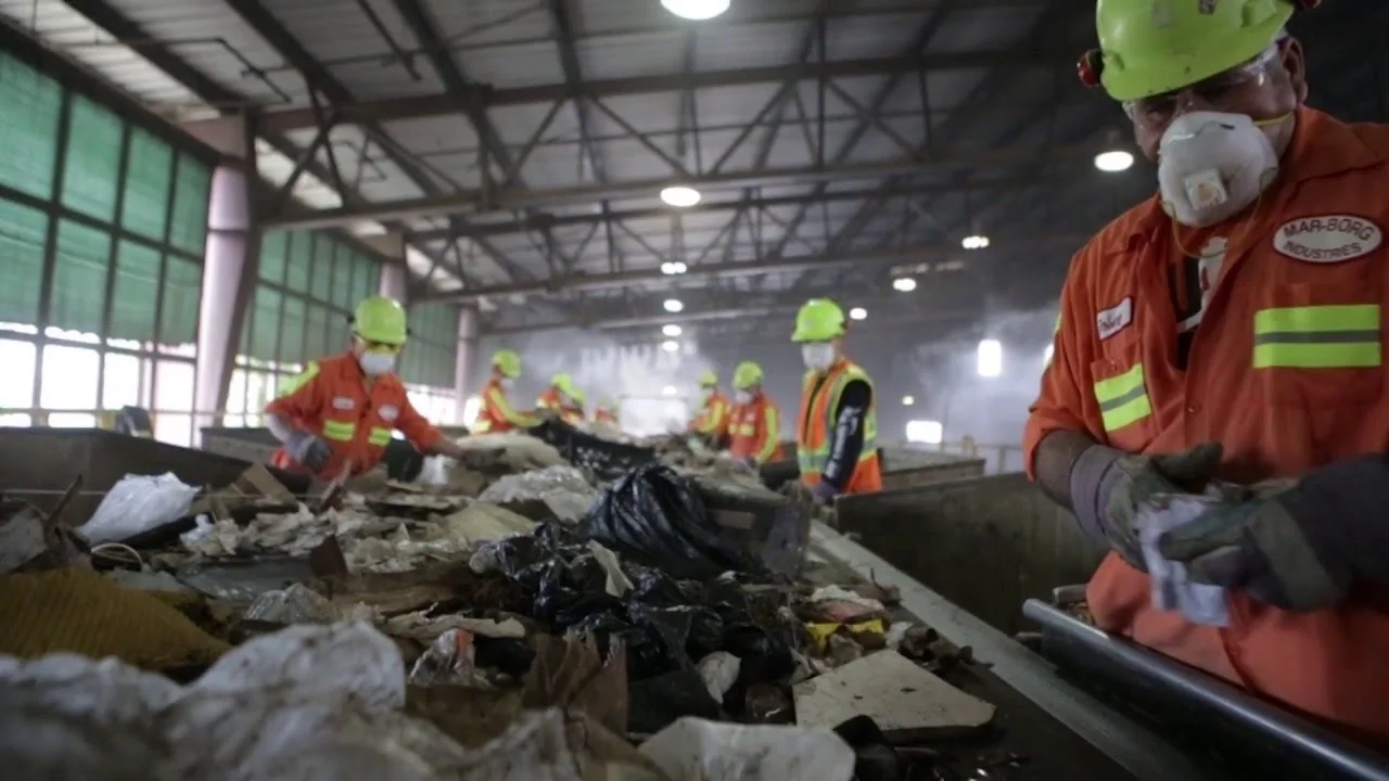 Workers in orange protective suits, helmets, masks, and gloves sorting through debris and trash at our recycling facility.