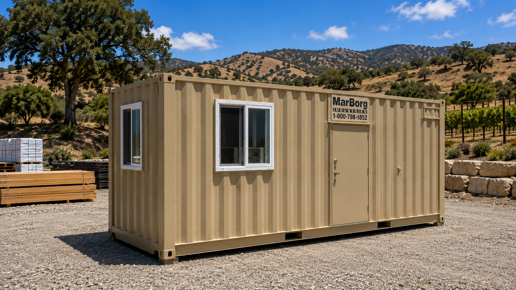 A beige shipping container with white window frames and a door, labeled 'MarBorg Industries,' situated outdoors with hills, trees, and a gravel ground in the background.