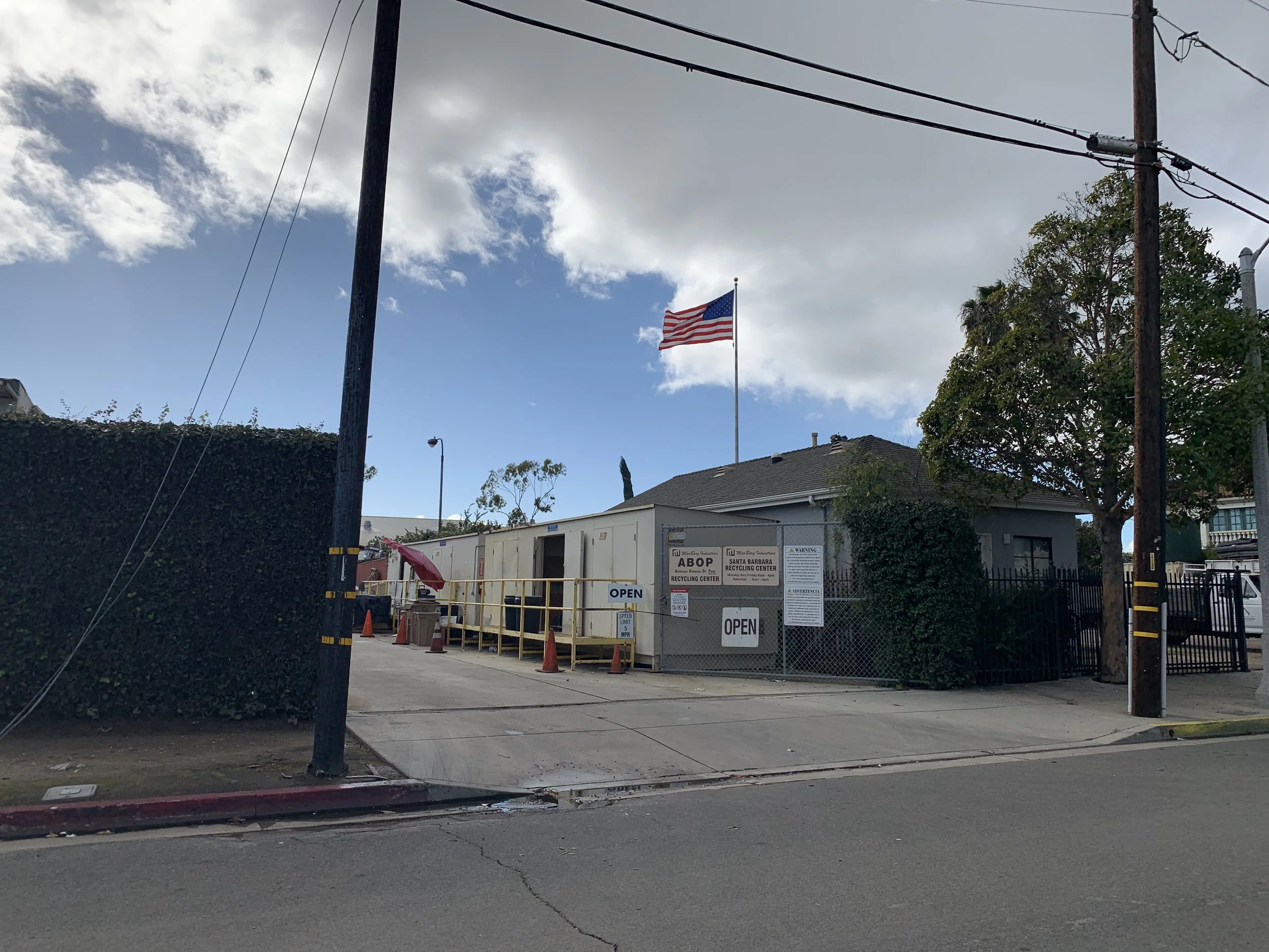 Front entrance view of the Anti-freeze Batteries, Oils and Paints (ABOP) Recycling Center. Tall American flag waiving overhead.