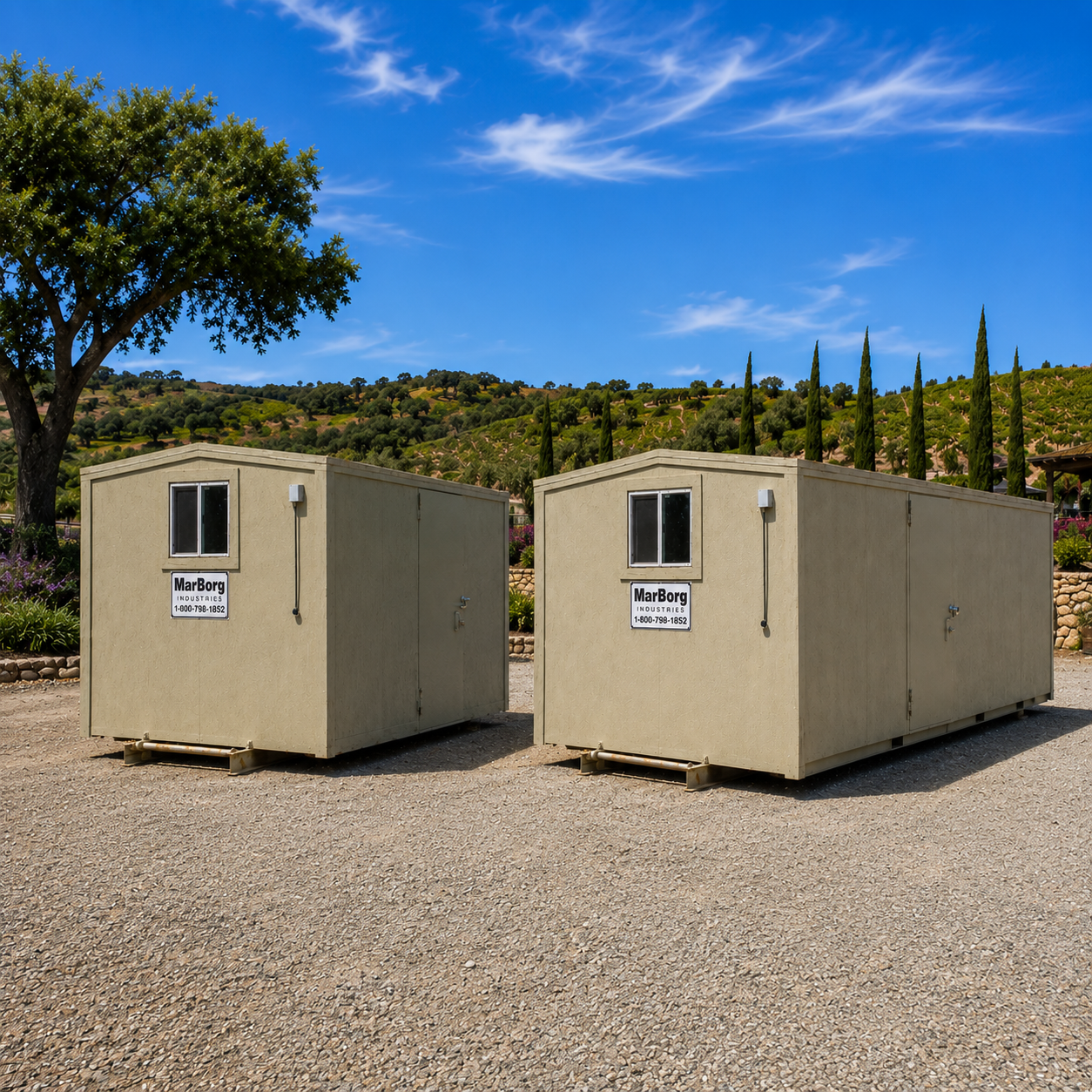 Two beige portable site offices on a gravel surface with trees and green hills in the background under a partly sunny sky.