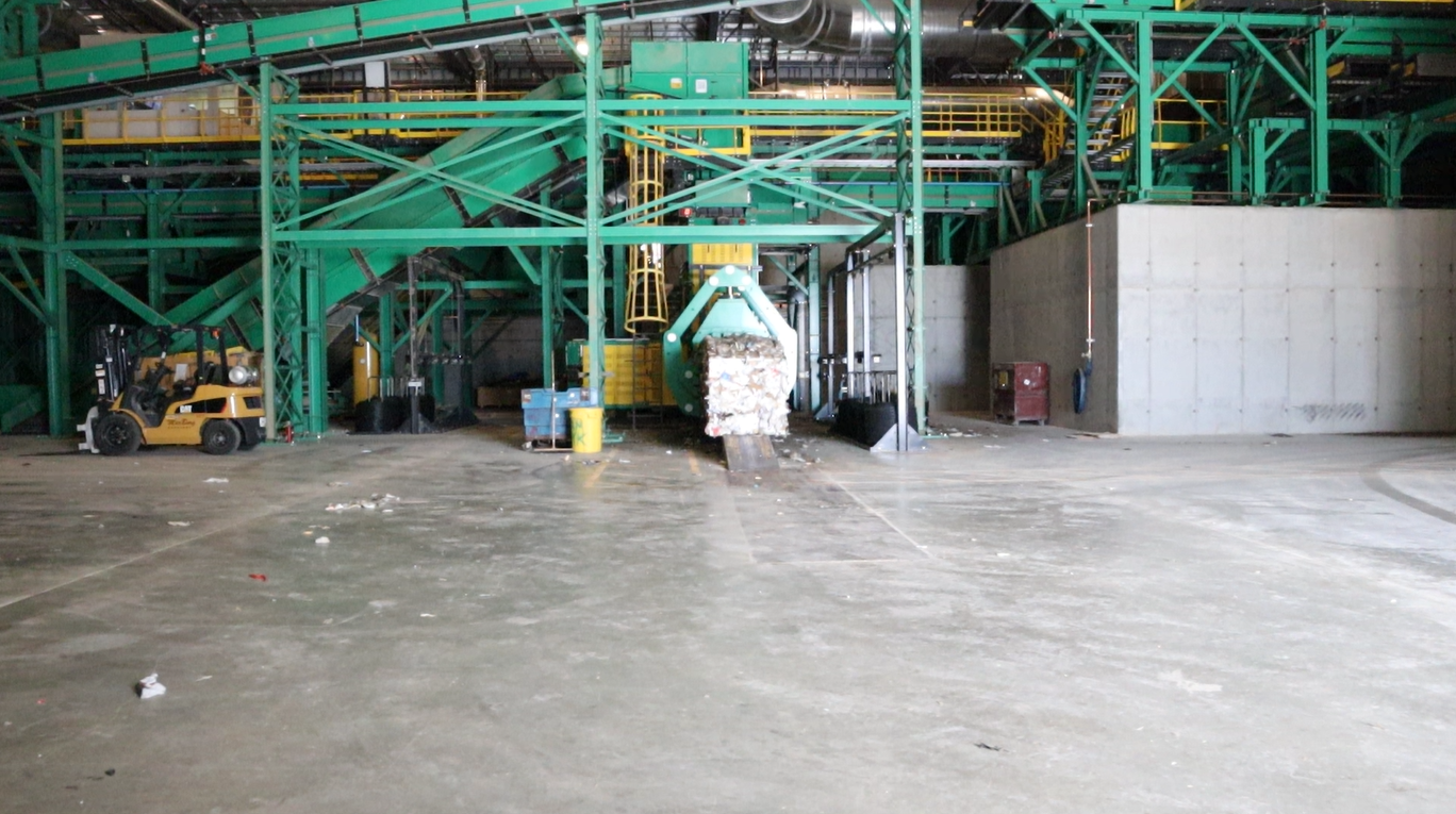 Industrial recycling facility with large green machinery, a forklift, and a pile of recyclable materials.