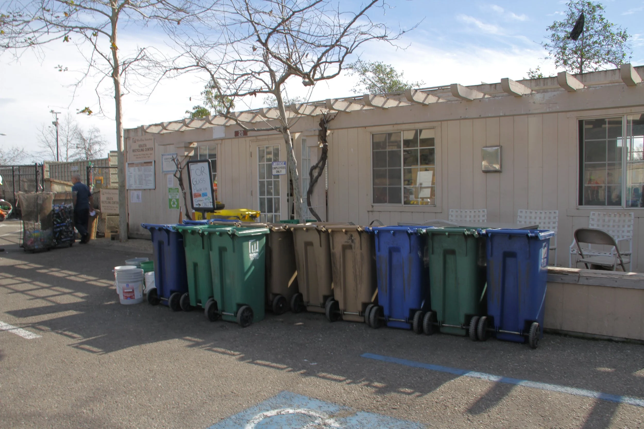 Front entrance to the David Love Recycling Center. Carts in the foreground with trees and the office building just behind.