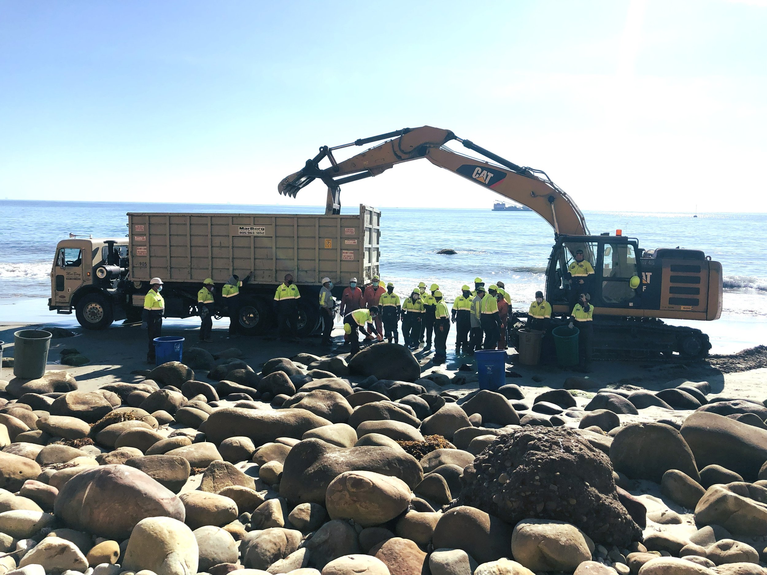 MarBorg team members utilizing an excalator and a 40yd roll-off container to  finish a beach cleanup following a boat coming ashore.