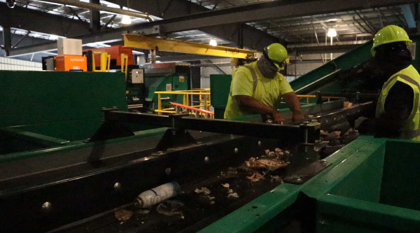 Workers in safety gear operating machinery in an industrial setting.