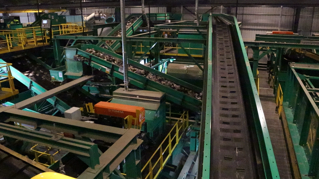 Industrial conveyor system with multiple green belts and yellow railings in a factory setting.