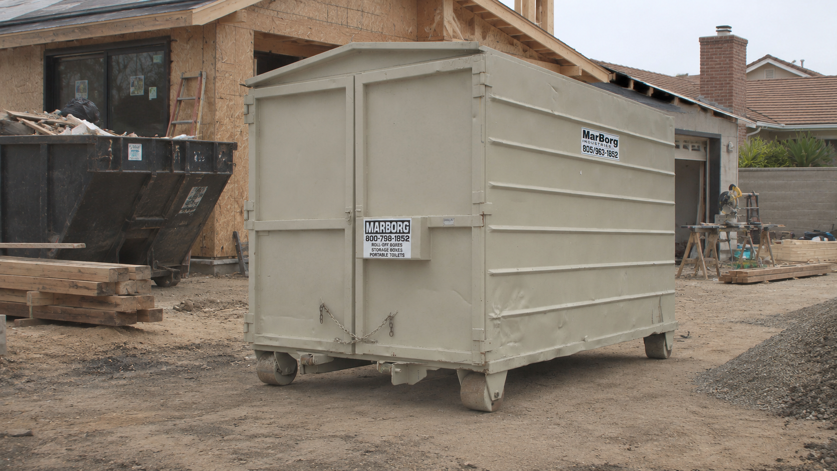 Construction site with a beige portable toilet, building materials, and equipment.