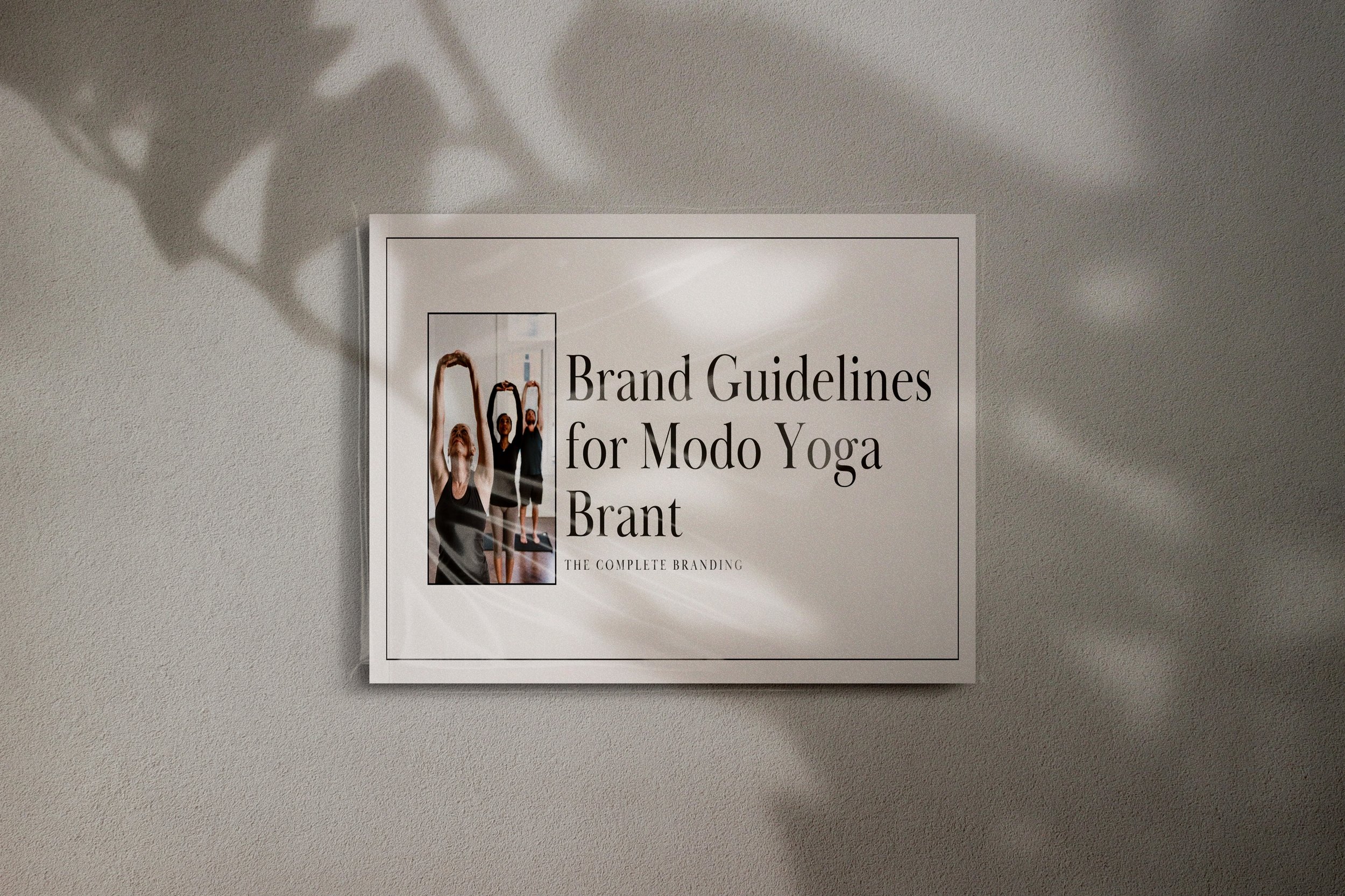 A printed guide titled 'Brand Guidelines for Modo Yoga Brant' pinned to a textured gray wall, with shadows cast by nearby objects.
