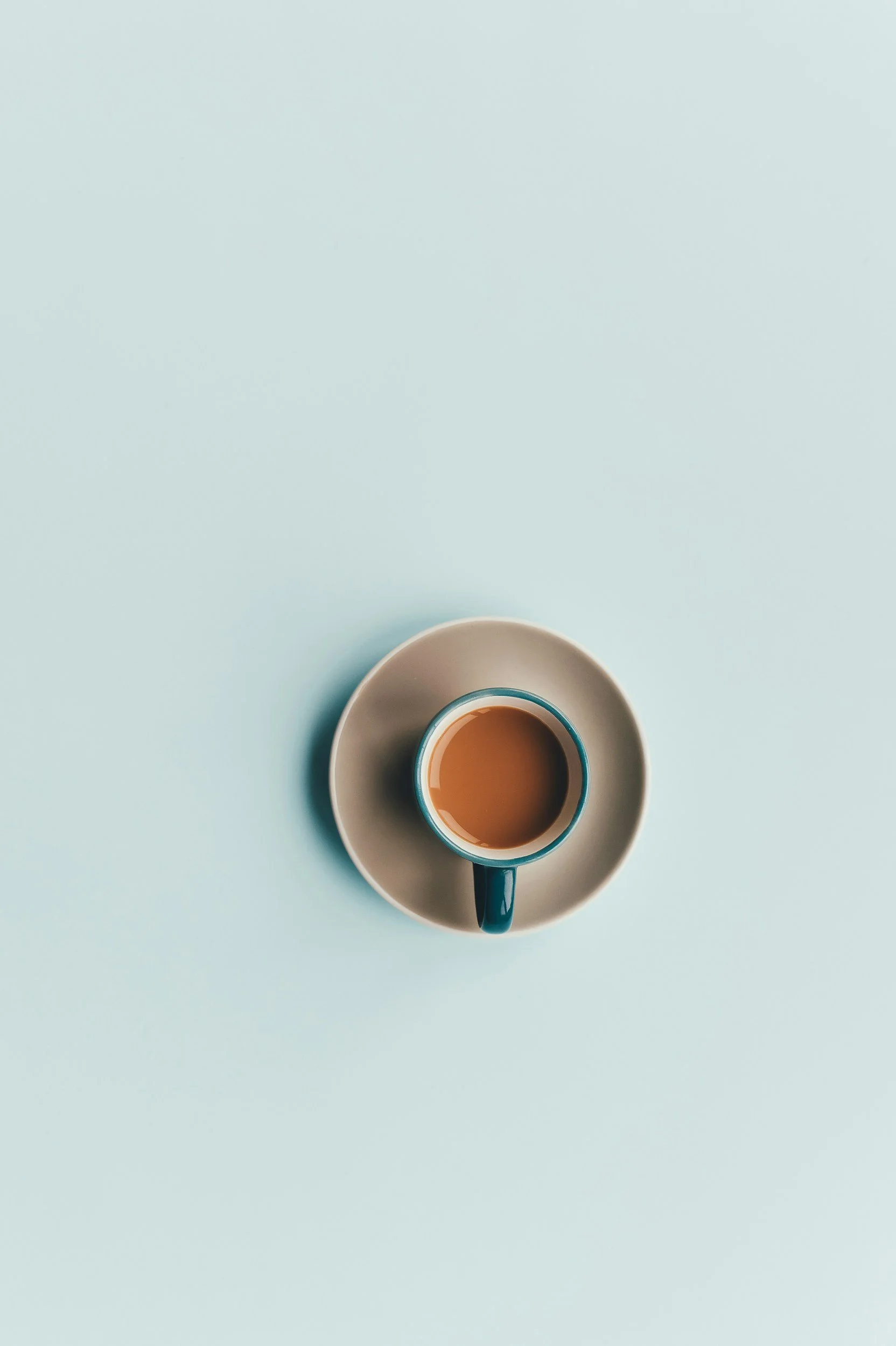 Top-down view of a blue mug filled with coffee on a white saucer against a light blue background.