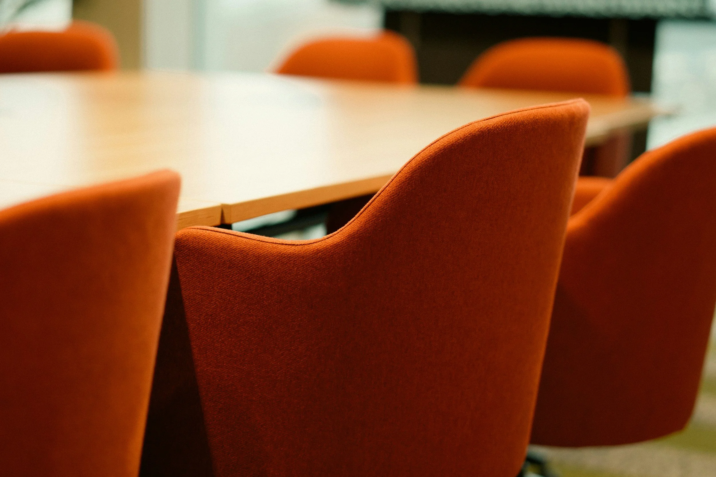 A close-up of several orange upholstered chairs surrounding a white conference table in a meeting room.