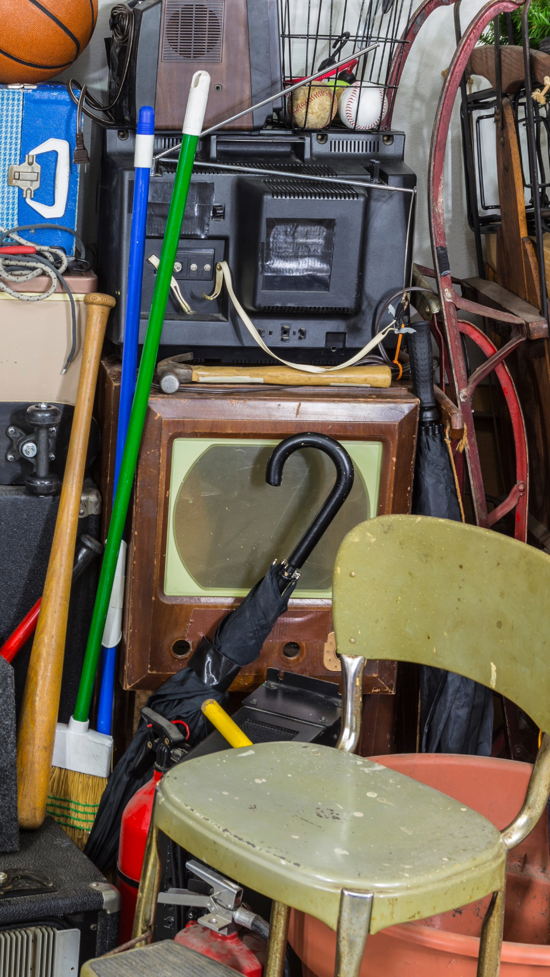 Cluttered storage room with vintage radio, baseballs, a golf club, a broom, chairs, and various miscellaneous items.