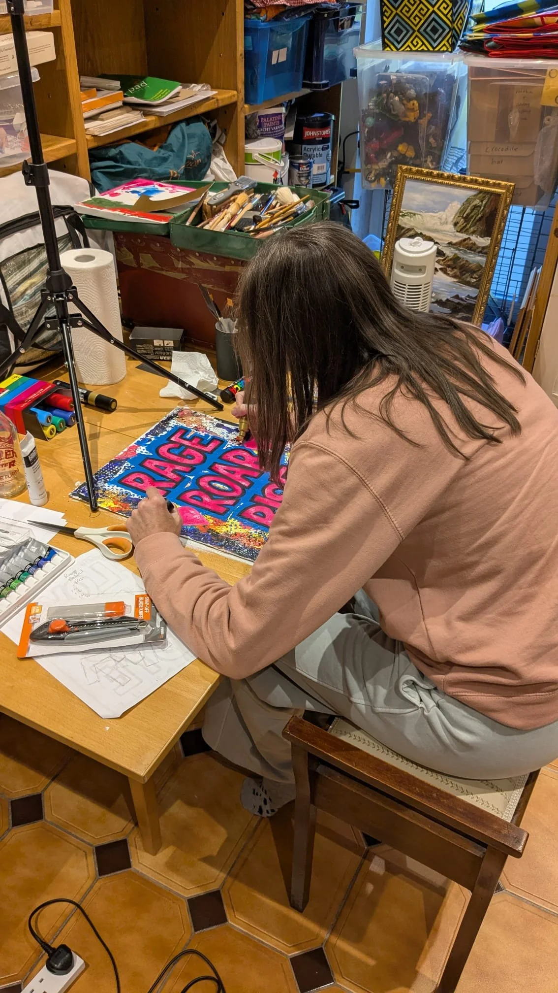Person working on a colorful sign that says 'PEACE PROGRESS' at a cluttered craft workspace.