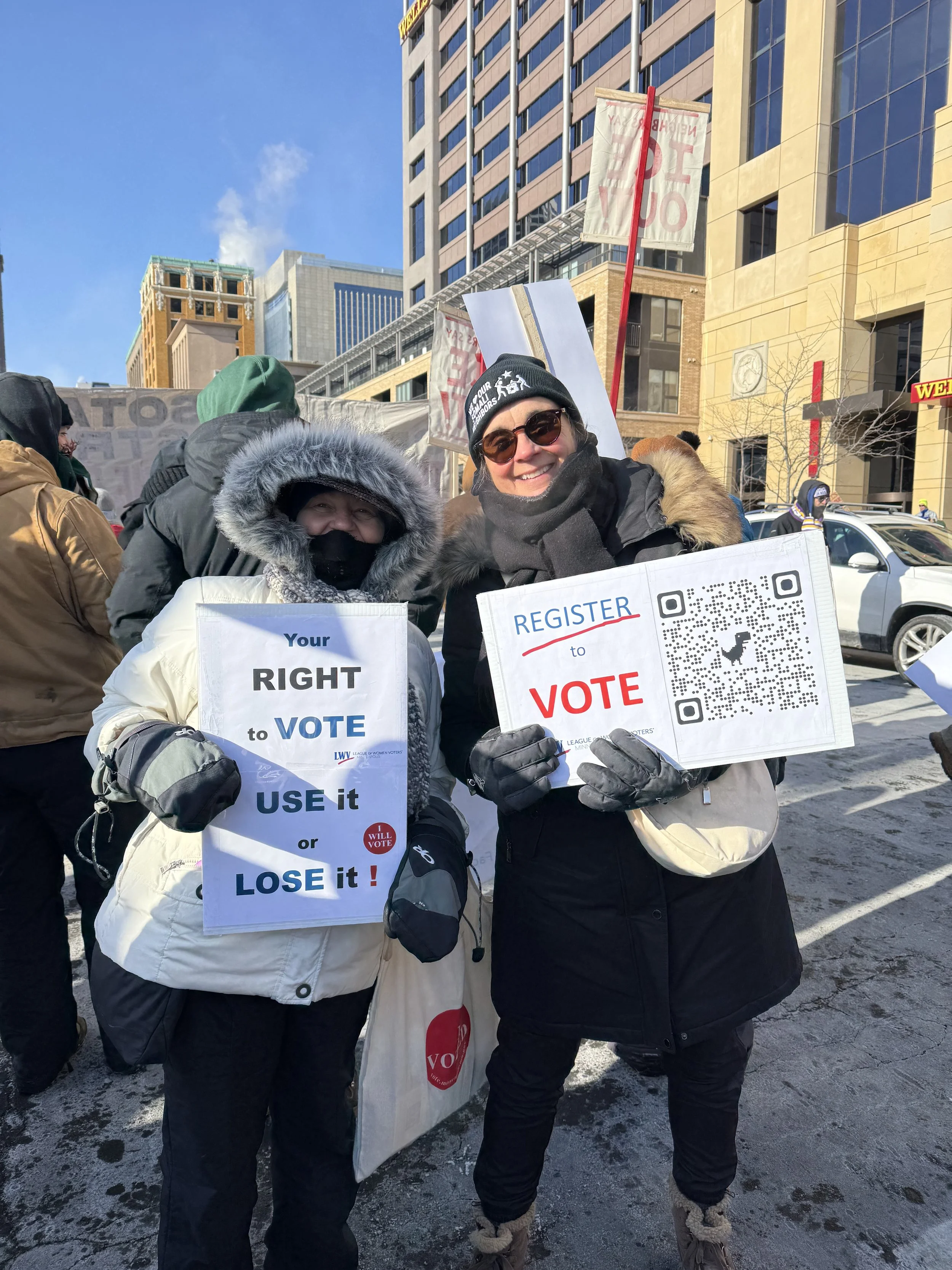 People participating in a protest or rally on a city street, holding signs that promote voting rights and civic engagement during winter.