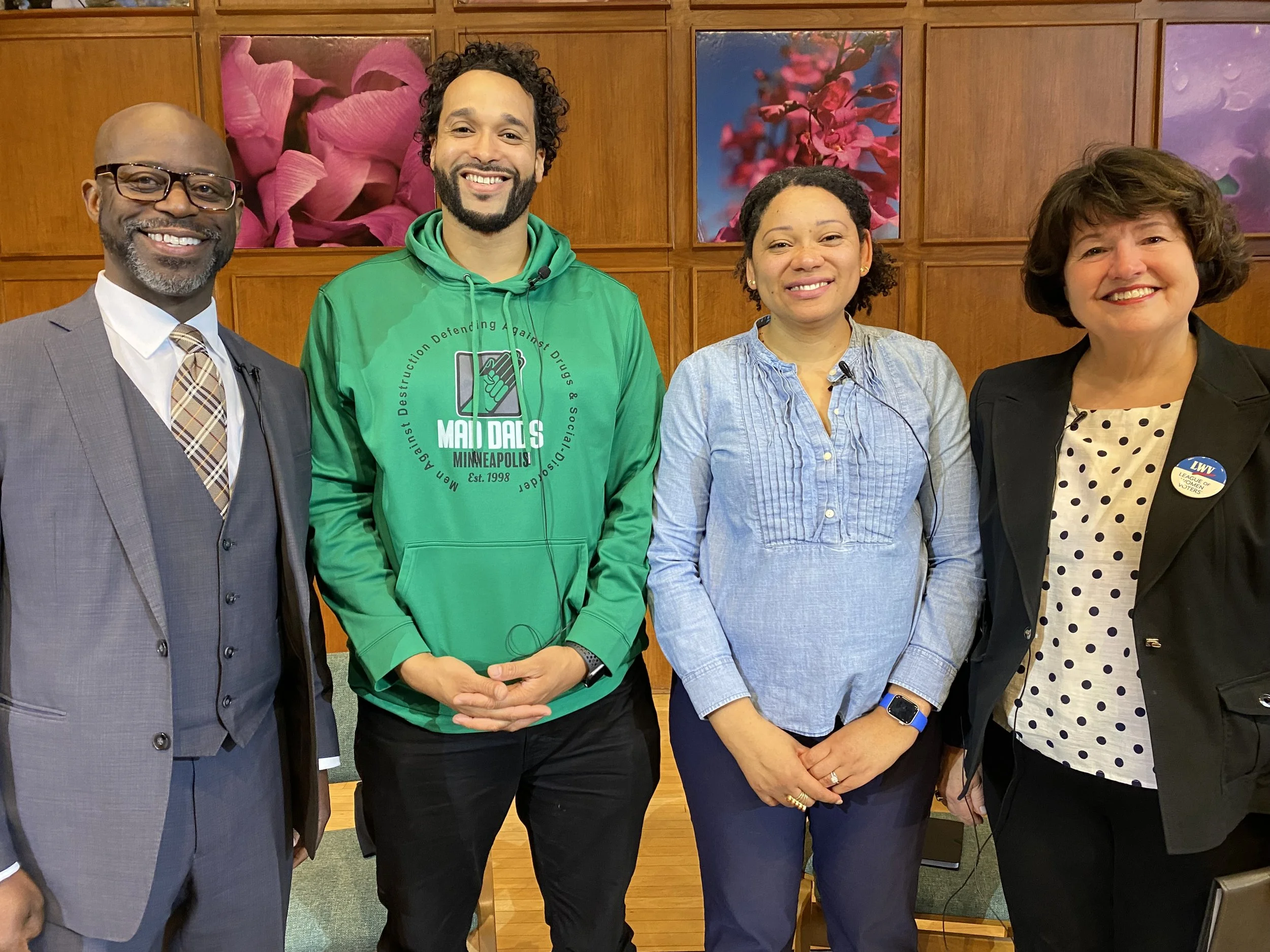Group of four diverse people standing together indoors, smiling, with colorful floral artwork in the background.