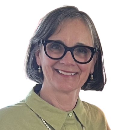 A smiling woman with shoulder-length gray hair wearing large black glasses, pearl earrings, a light green collared shirt, and a pearl necklace.