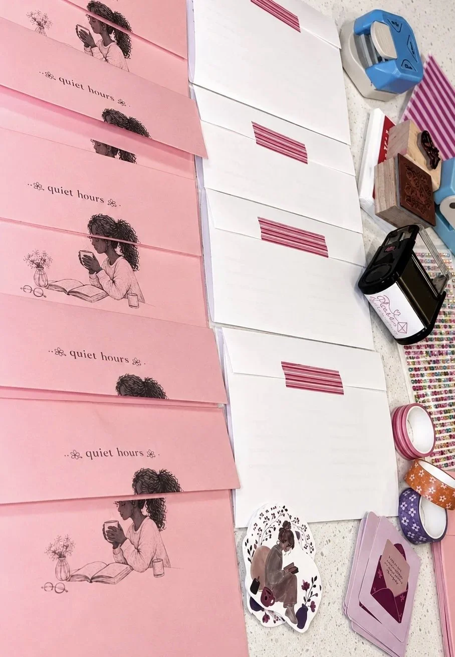 Pink envelopes with a woman reading a book on them, white blank cards with red striped tape, various decorative tapes, a stamp and stamp pad, a round sticker with a girl reading a book, and a small pile of pink cards.