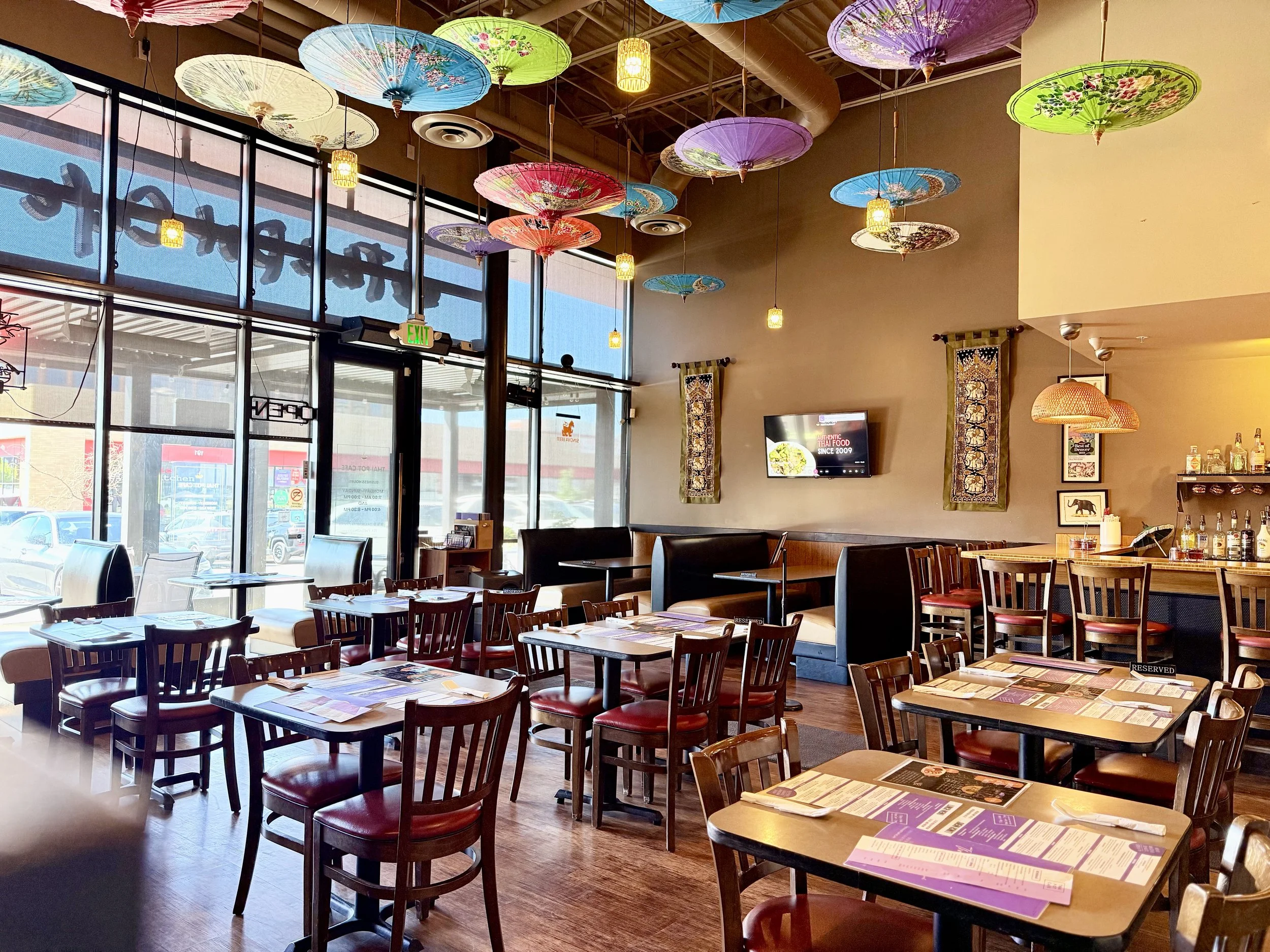 Thai imported colorful instagram worthy paper umbrellas adorn the ceiling of a beautiful full glass front indoor restaurant. many tables, booths, bar, and an outdoor pergola with chairs. dine in or take out. cozy, bright, shade, screens, heaters