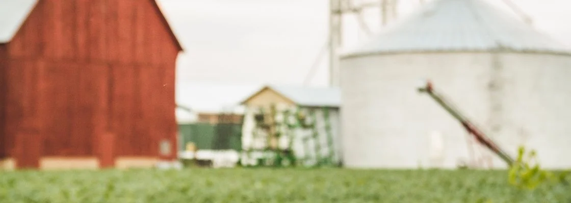 Blurred farm scene with red barn, green shed, and white silo