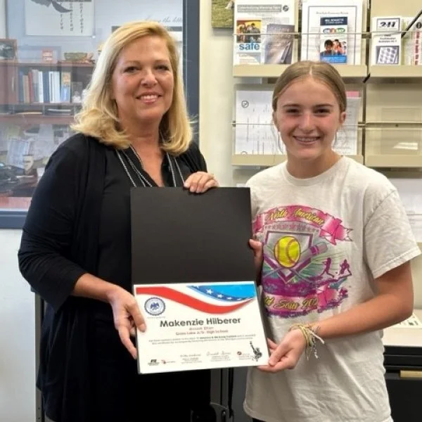 A woman and a girl holding a certificate together and smiling in an office or store setting.