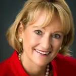 Close-up of a smiling woman with short blond hair wearing pearl earrings and a red top