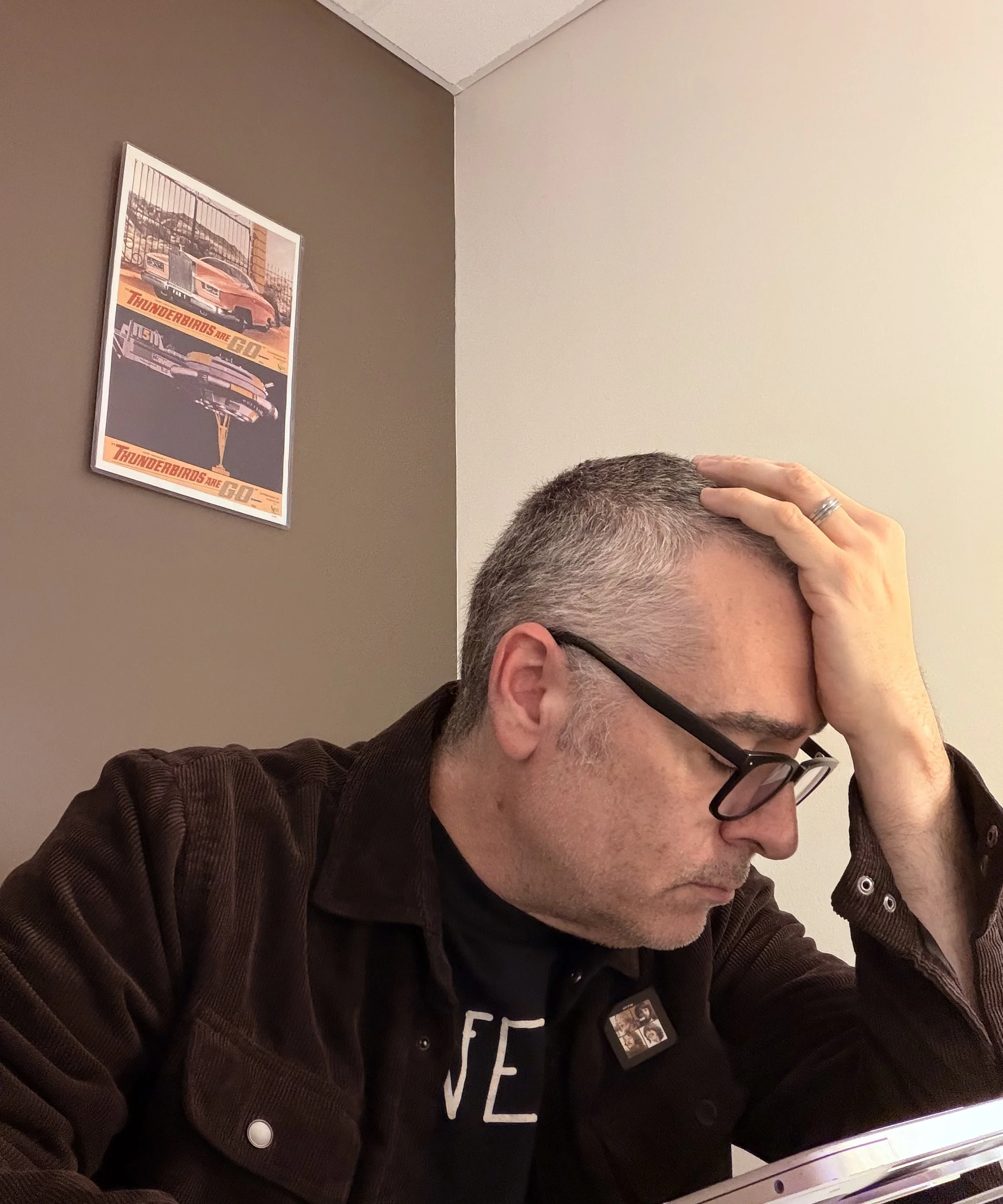 A man sits thoughtfully at his laptop