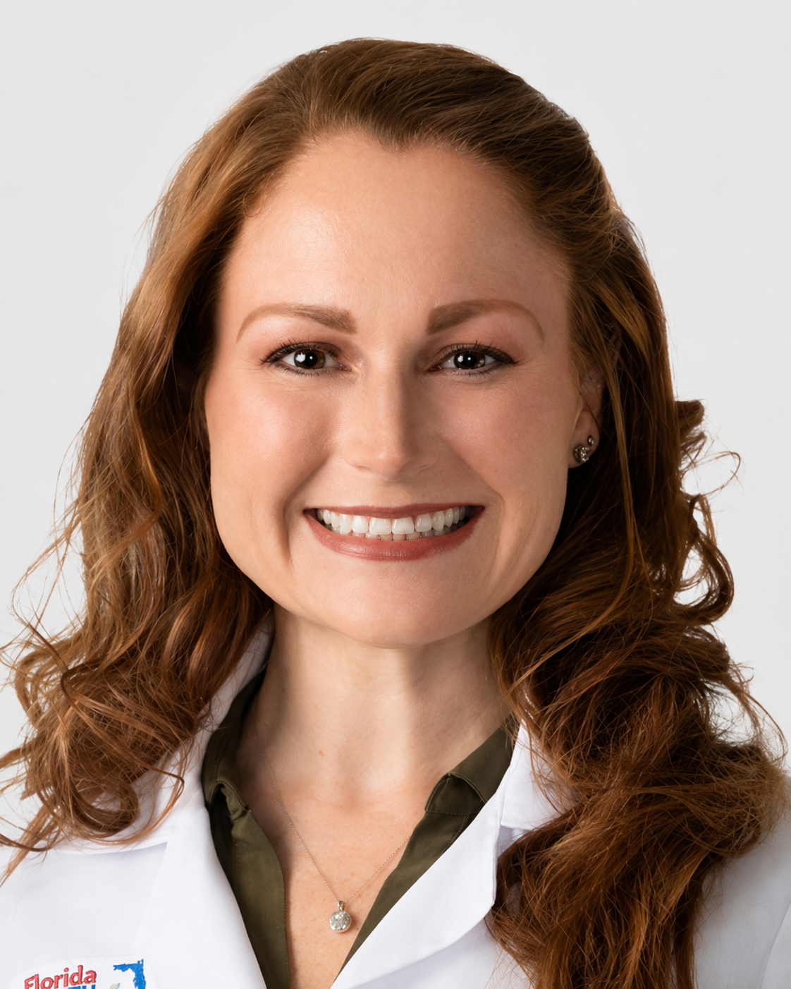 Close-up of a woman with red curly hair smiling, wearing a white shirt and a pendant necklace.