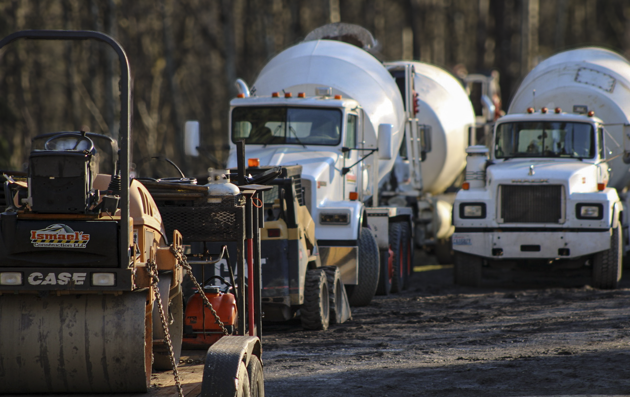 Multiple cement mixer trucks parked outdoors on a construction site with trees in the background.