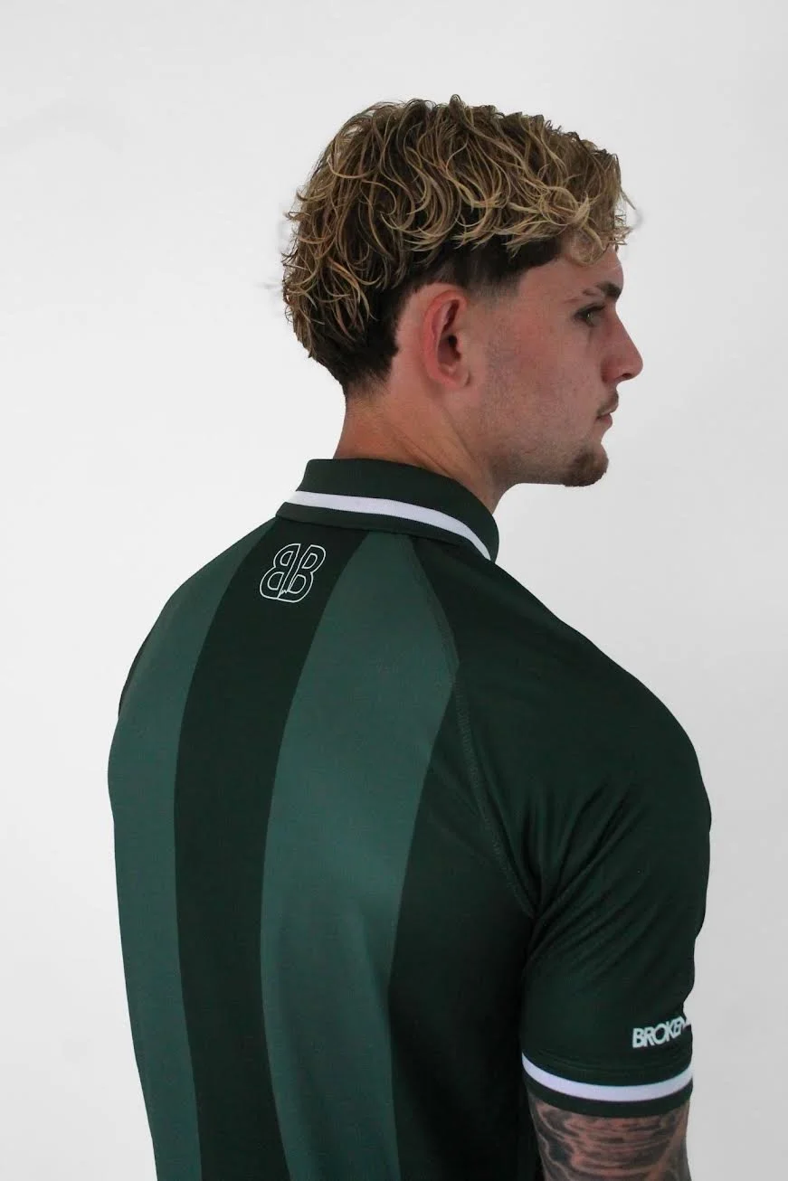 Side profile of a young man with styled blond curly hair, wearing a black and green sports jersey with white accents, standing against a plain white background.