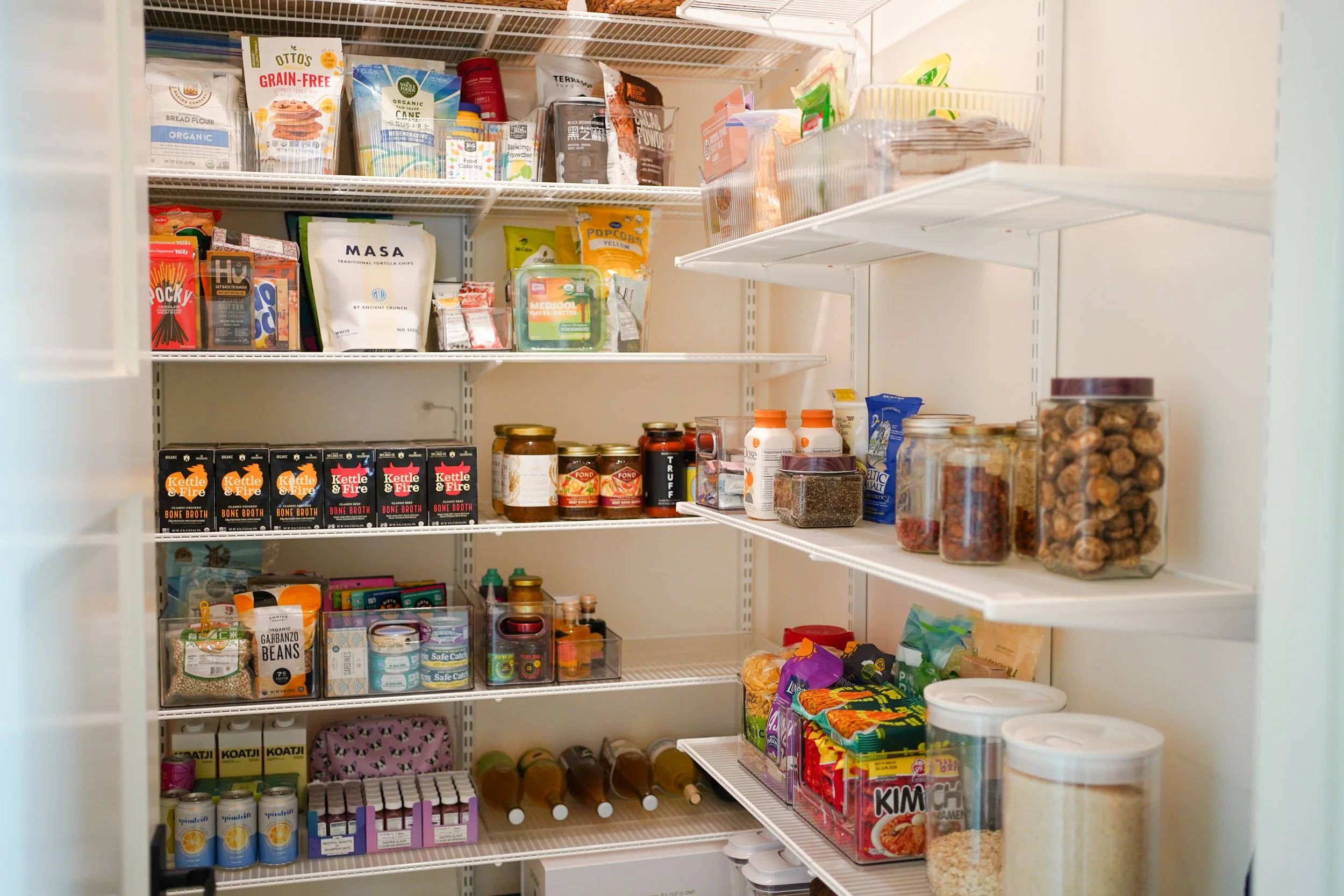 Inside of a pantry with shelves containing various food items including snacks, canned goods, and packaged foods. Organized neatly with order and functionality.