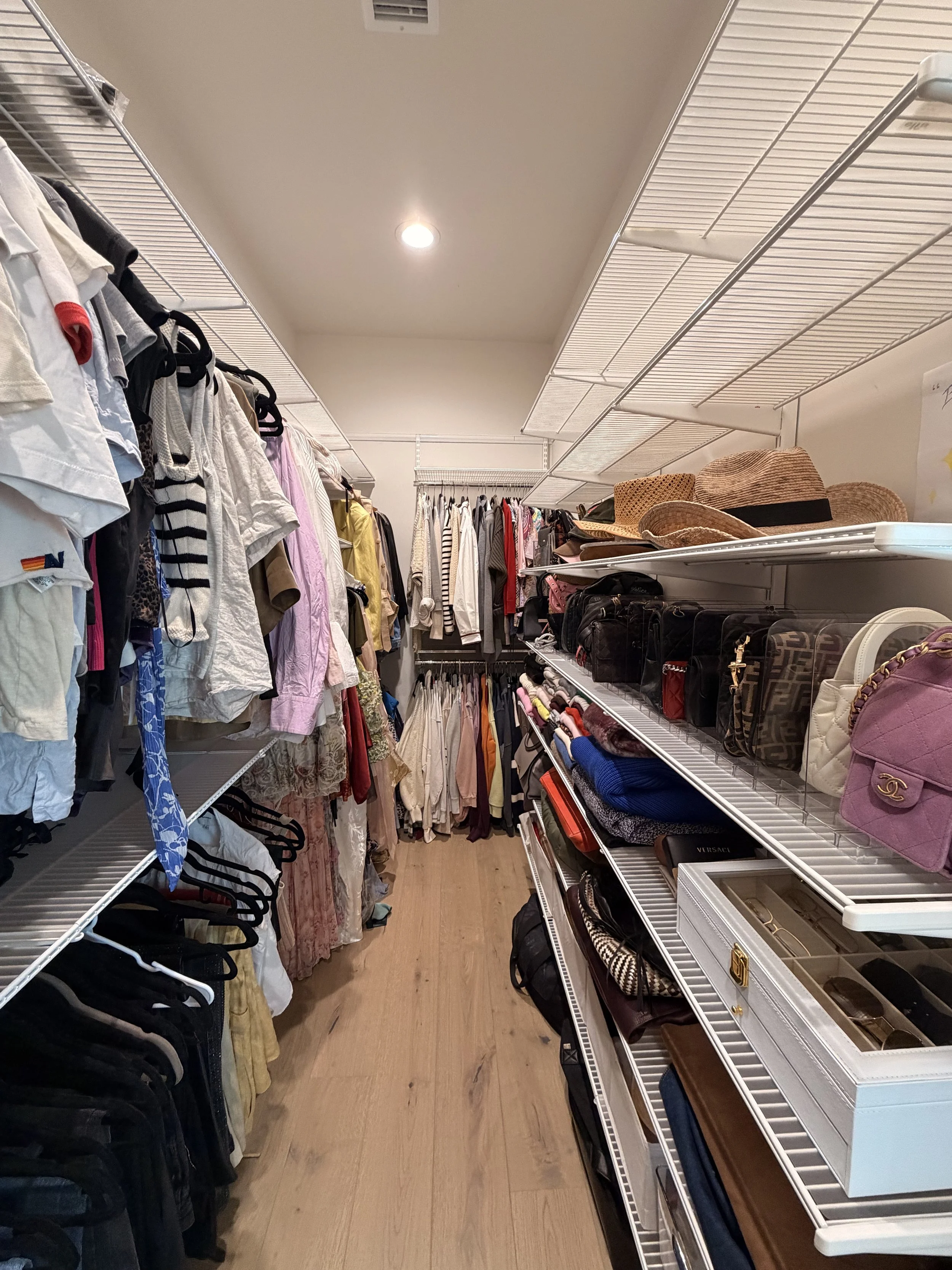 A narrow aisle in a resale clothing store with racks of shirts, pants, hats, and handbags on either side.