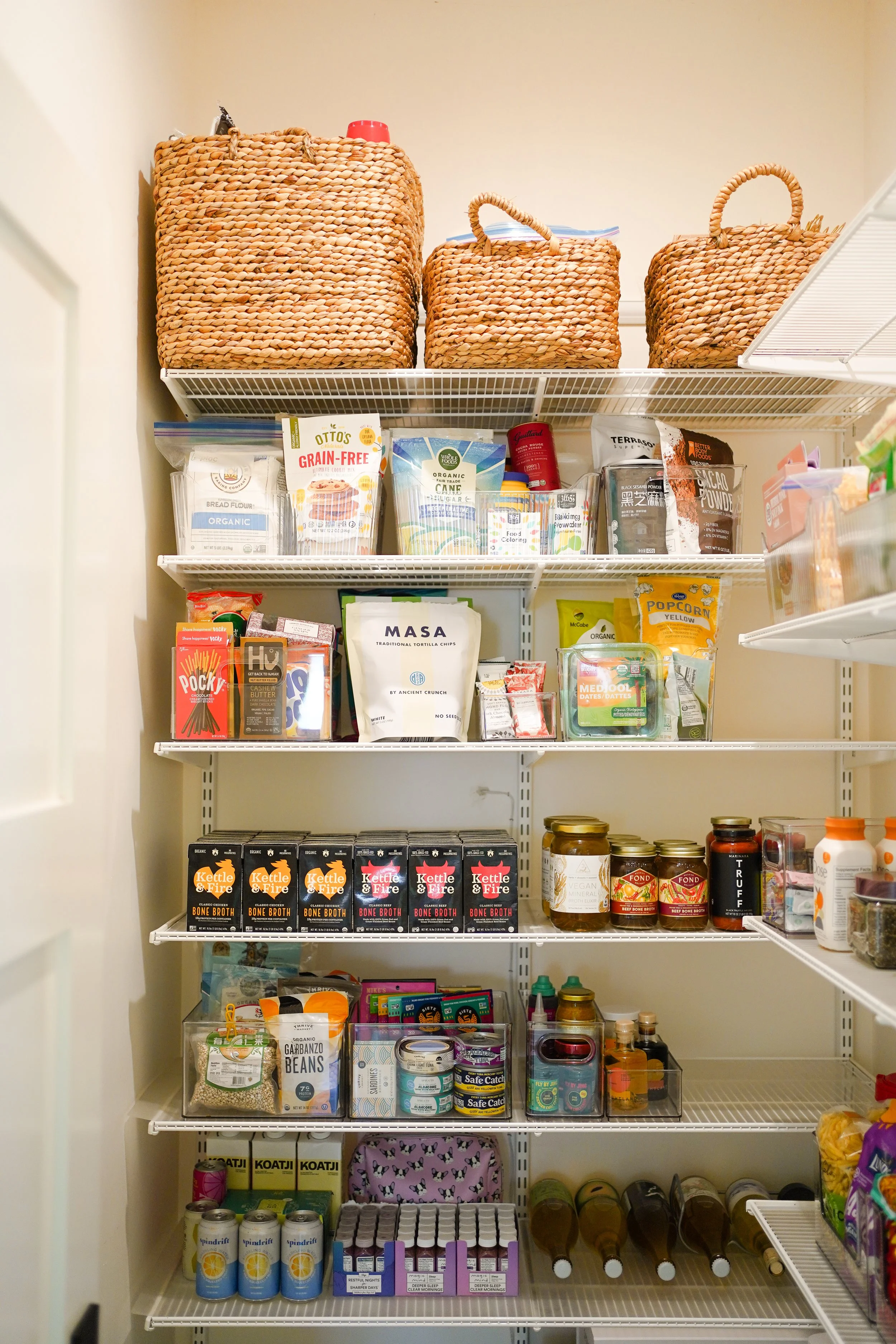 A pantry with four shelves filled with various food and drink items, including boxes, jars, cans, and bottles.
