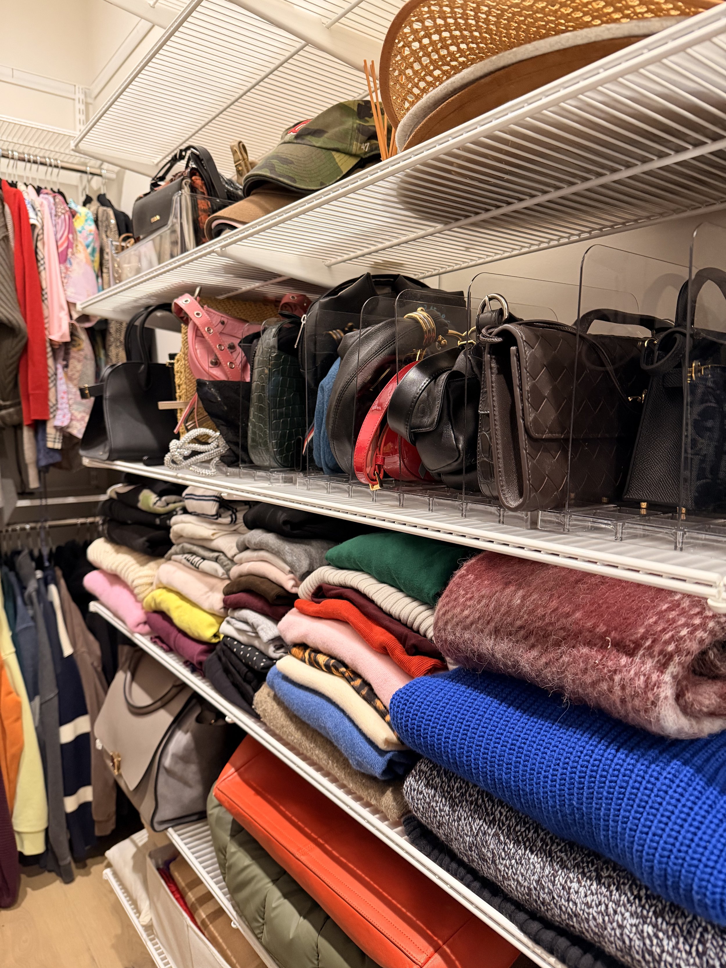 Shelves in a client's closet displaying folded sweaters, handbags, hats, and accessories.