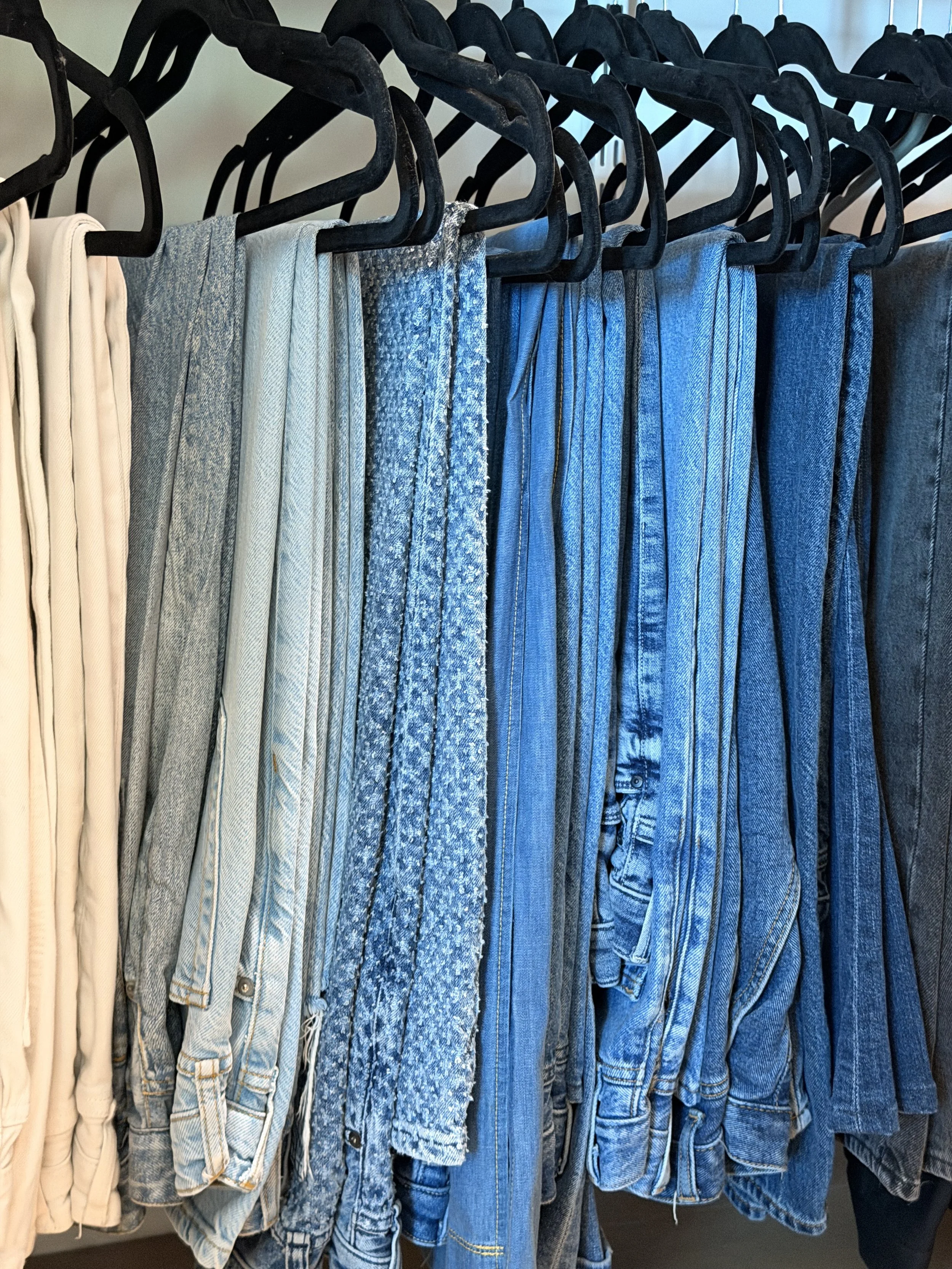 A row of denim jeans hanging on black plastic hangers on a clothing rack.